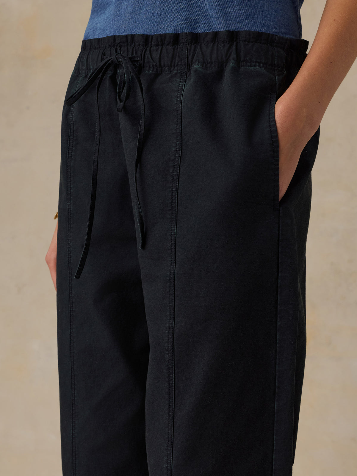 Woman wearing a blue t-shirt and black drawstring pants against a beige background, image 5 of 5