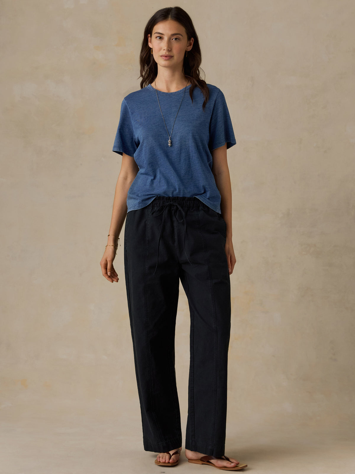 Woman wearing a blue t-shirt and black drawstring pants against a beige background, image 1 of 5