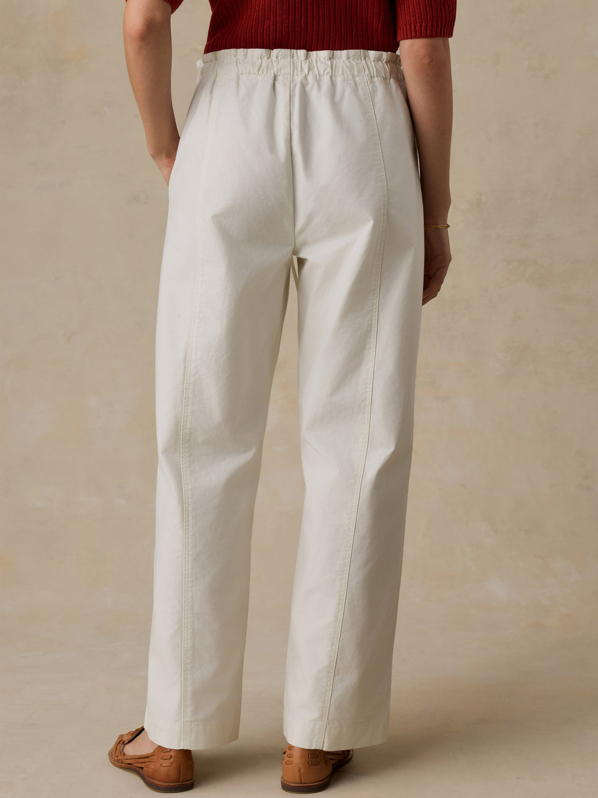 Woman wearing a red knit polo shirt and white drawstring pants against a beige background, image 5 of 6