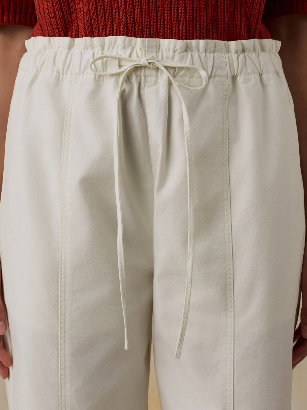 Woman wearing a red knit polo shirt and white drawstring pants against a beige background, image 6 of 6