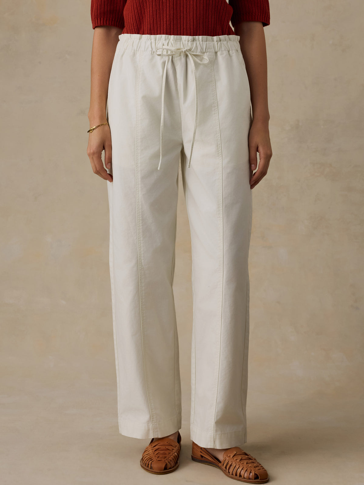 Woman wearing a red knit polo shirt and white drawstring pants against a beige background, image 2 of 6