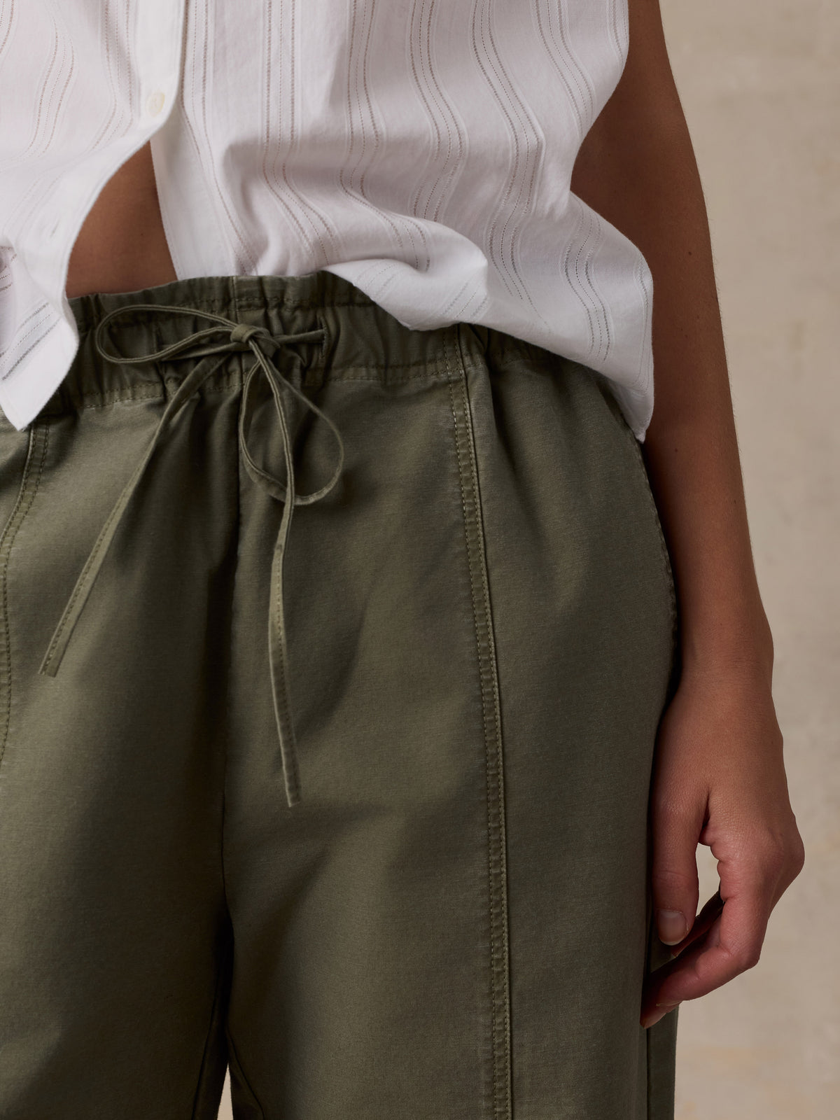 Close-up of a woman wearing a white blouse and olive green pants against a beige studio background, image 5 of 5
