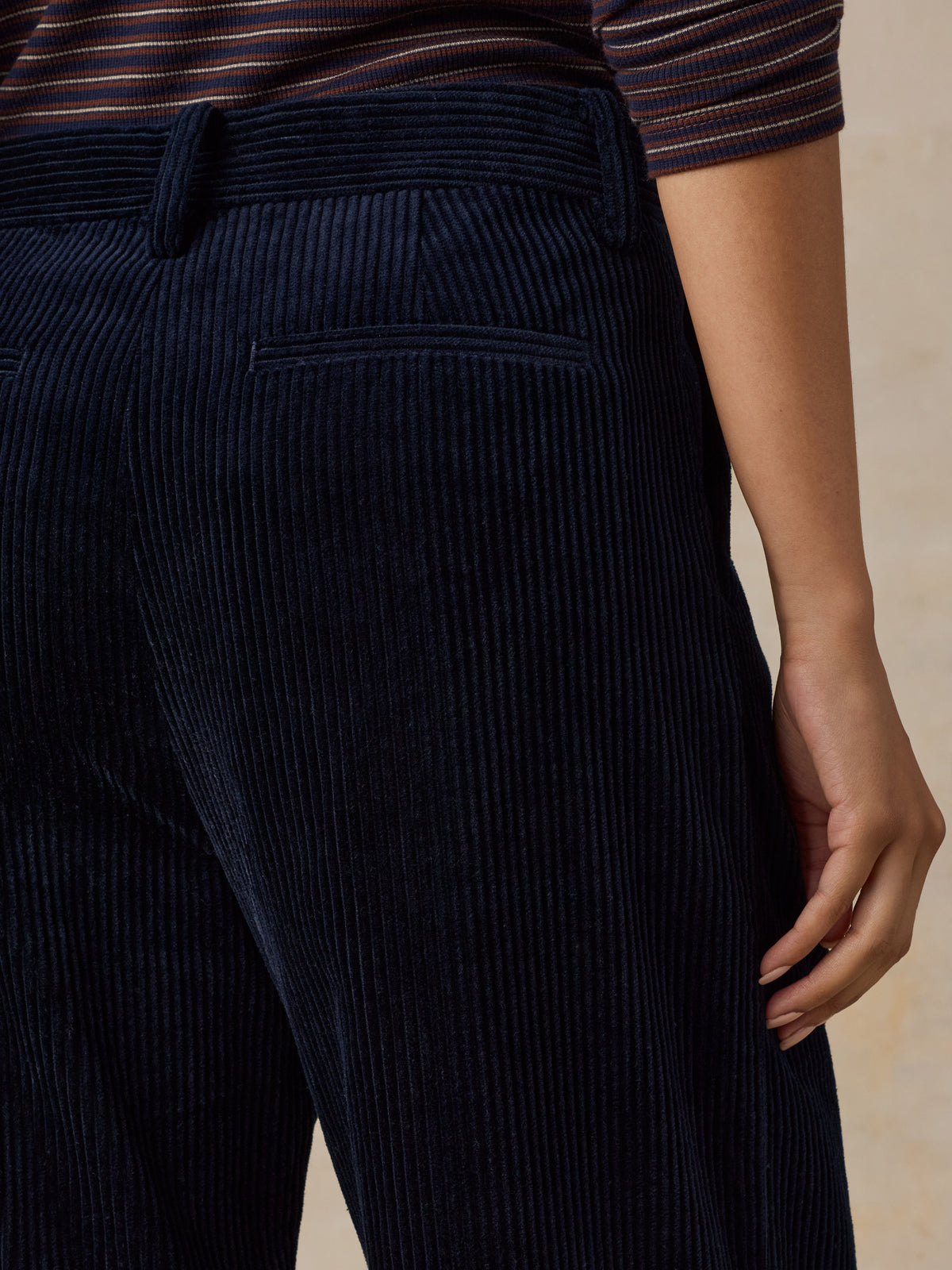 Close up of a woman viewed from behind wearing dark navy blue corduroy pants and a striped top, image 6 of 7