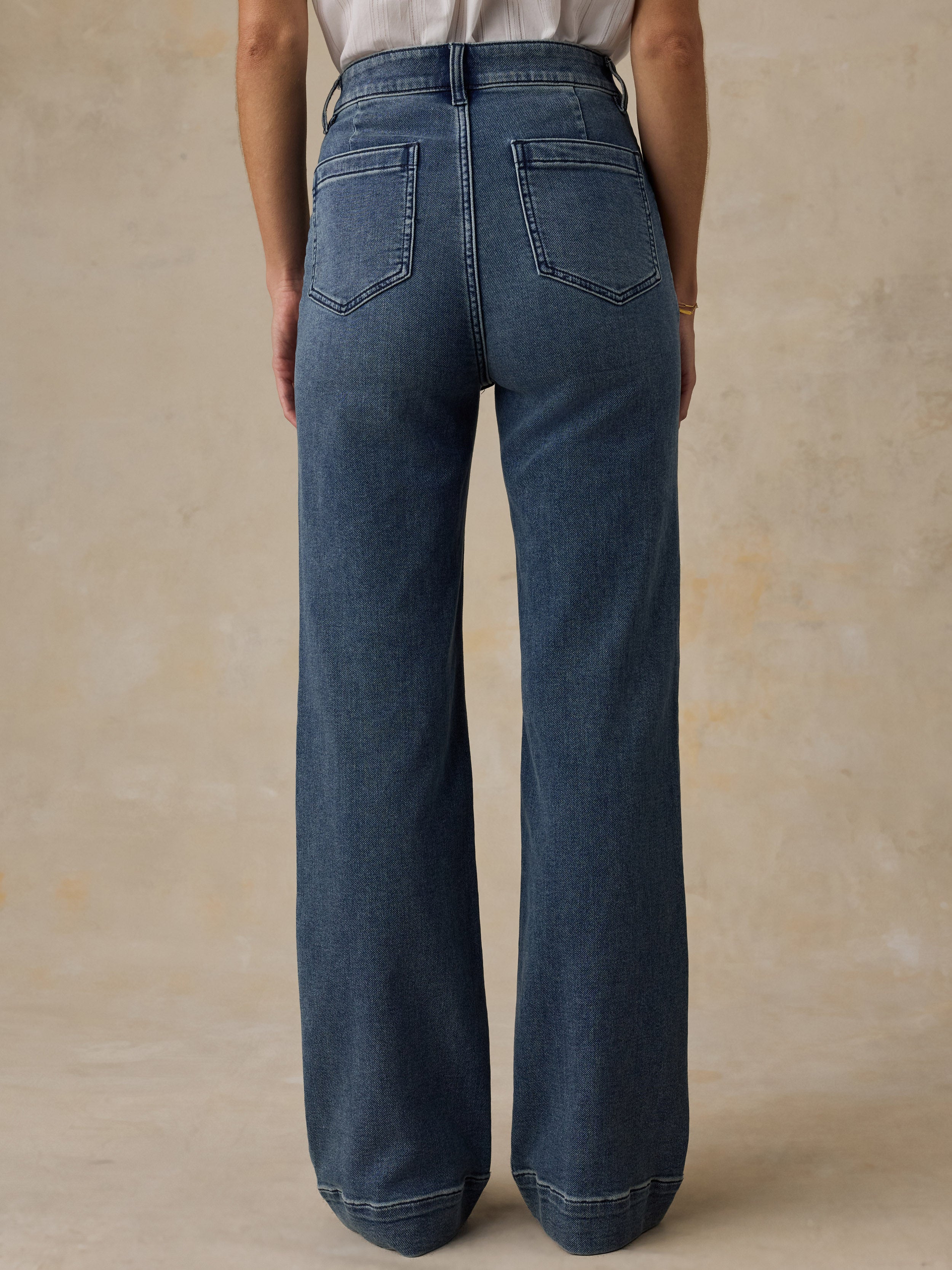 Woman wearing a white top and high waisted blue jeans against a beige background