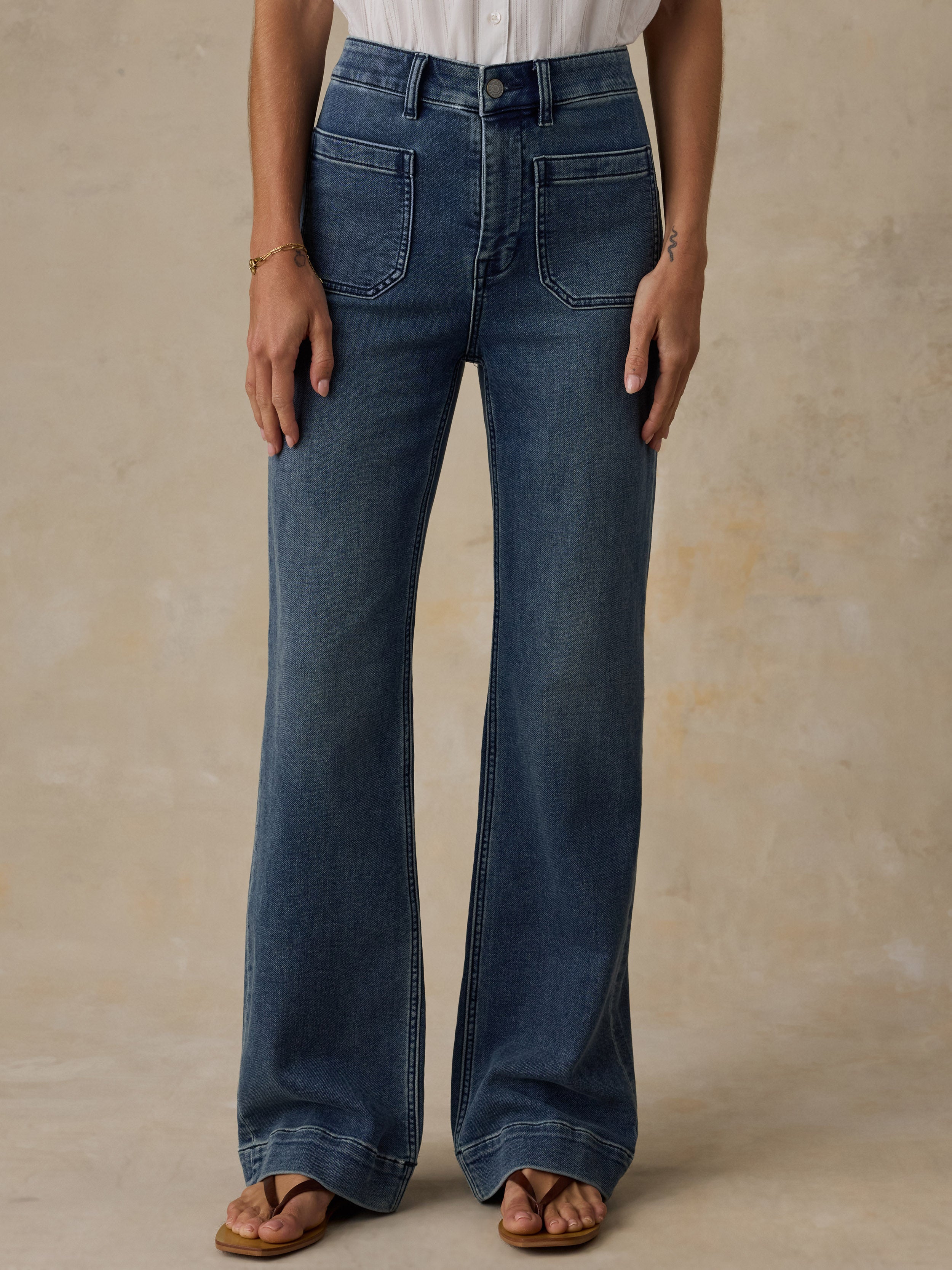 Woman wearing a white top and high waisted blue jeans against a beige background