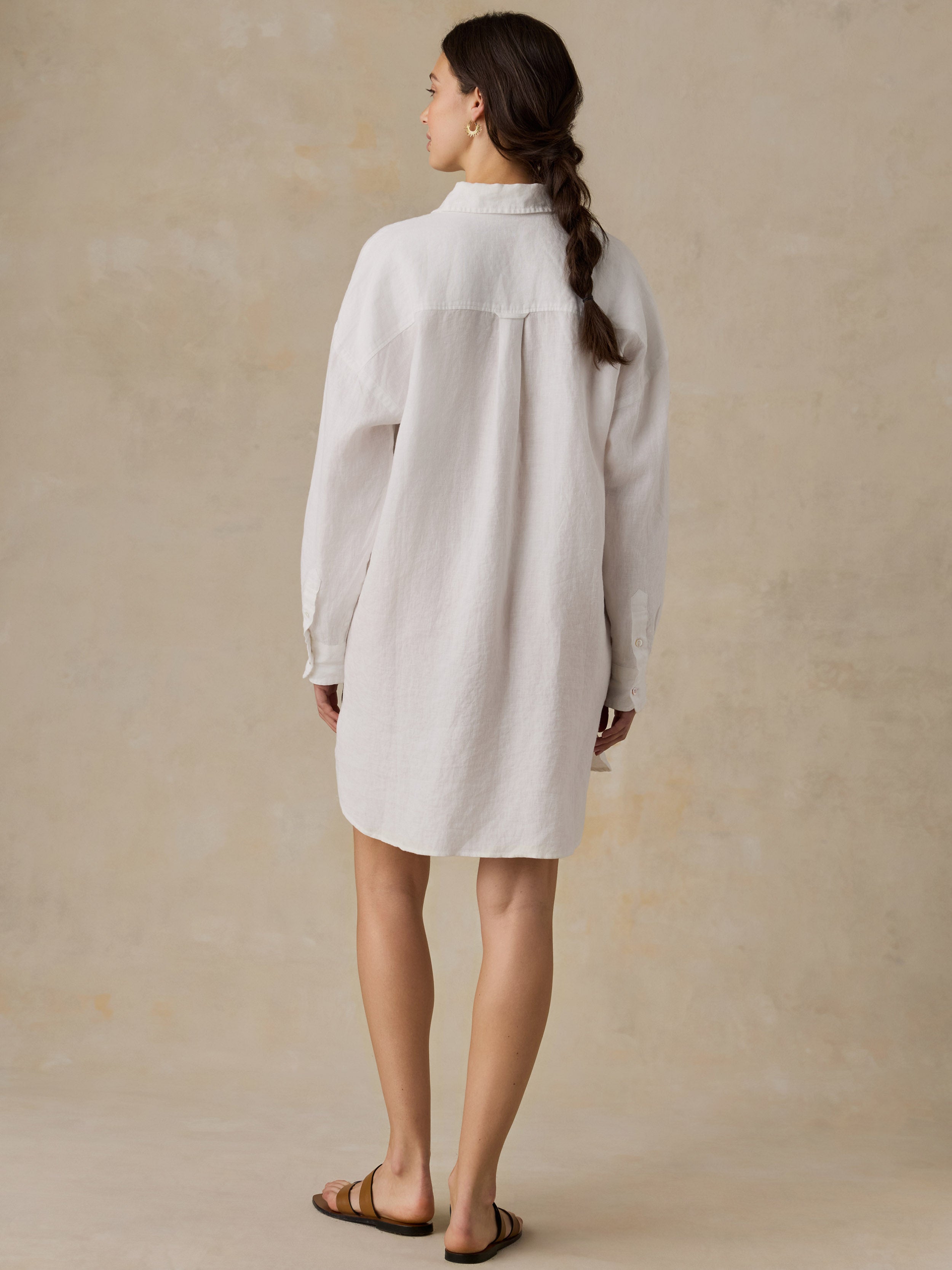 Woman wearing a white linen shirtdress against a beige background