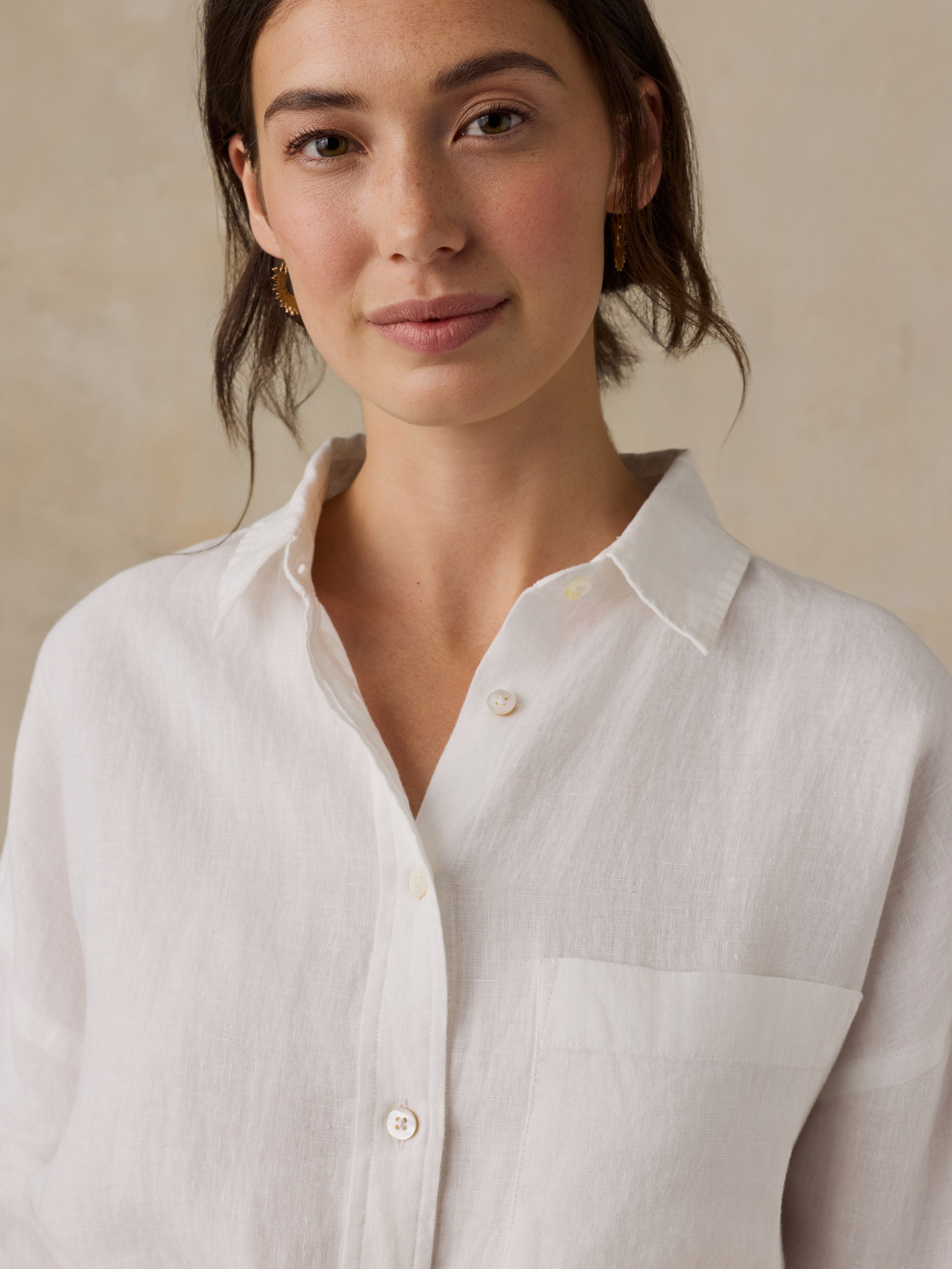 Woman wearing a white linen shirtdress  against a beige background