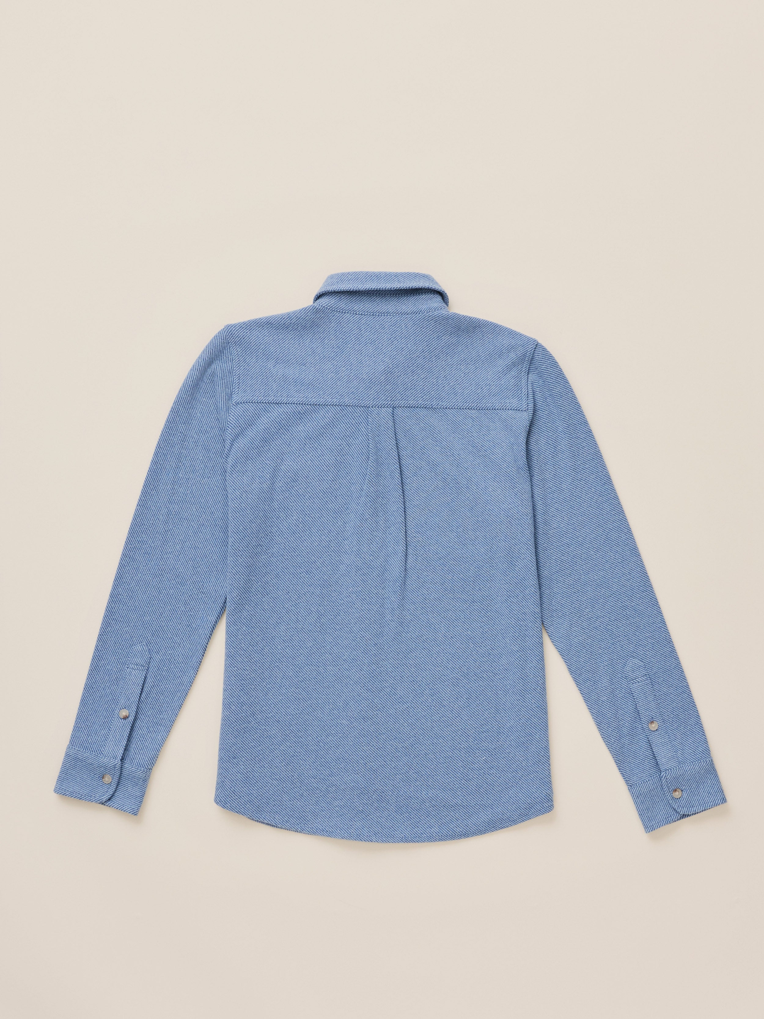 A light blue long-sleeve button-up shirt shown from the back, laid flat on a warm beige background.