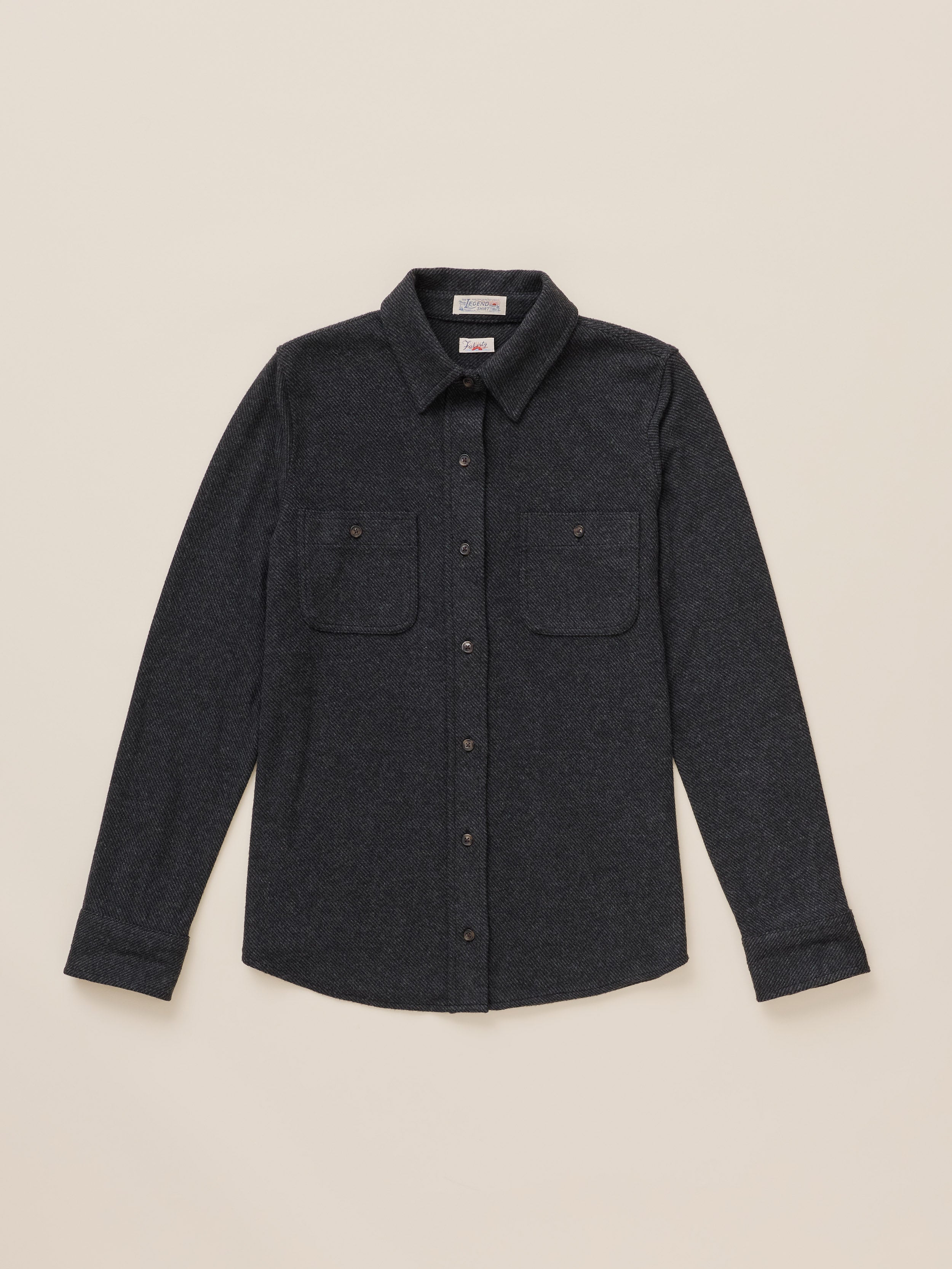 A dark charcoal gray long-sleeve button-up shirt with two buttoned chest pockets, laid flat against a light beige background.