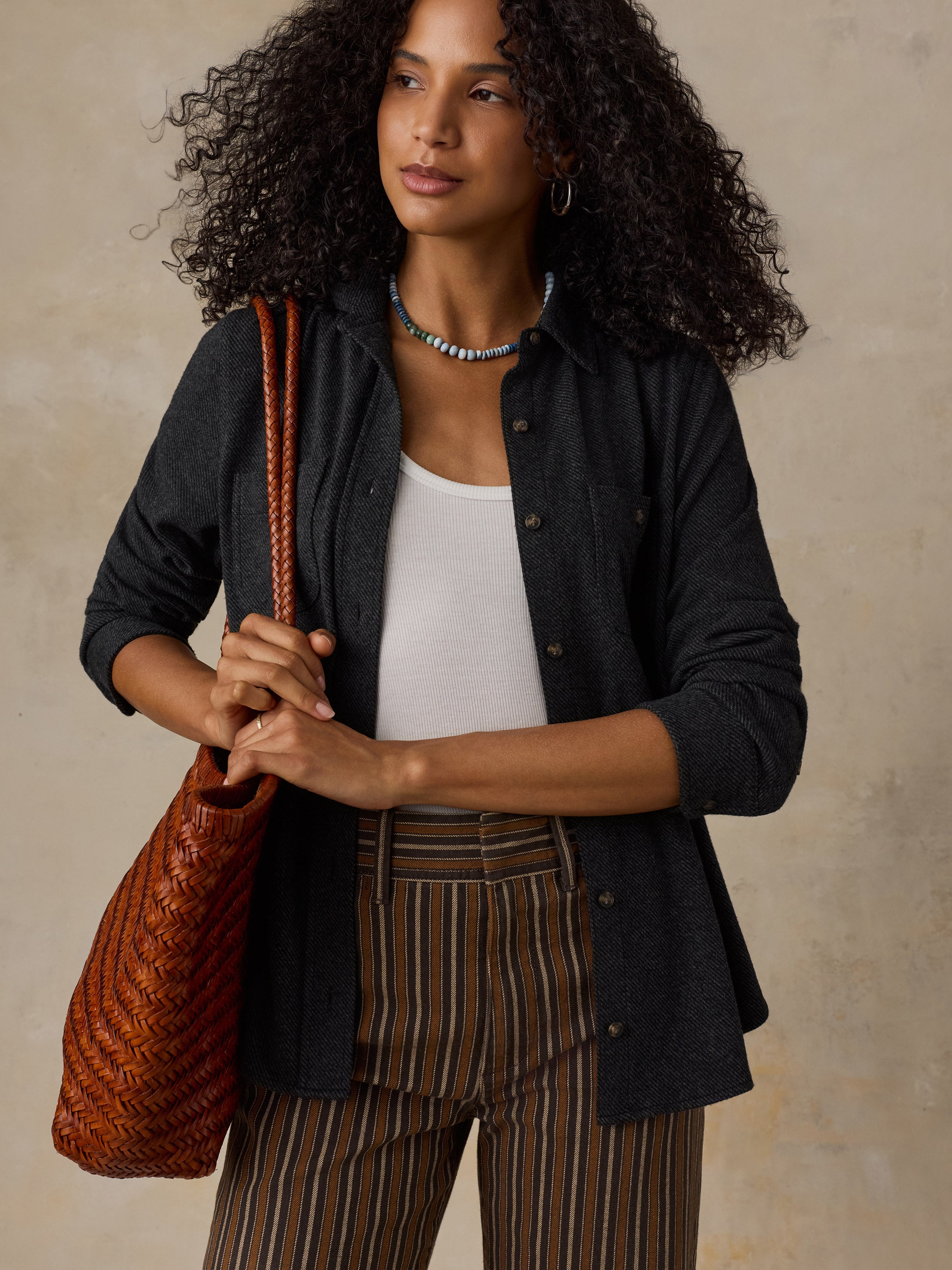 Woman wearing a black sweater shirt with brown striped pants against a beige background
