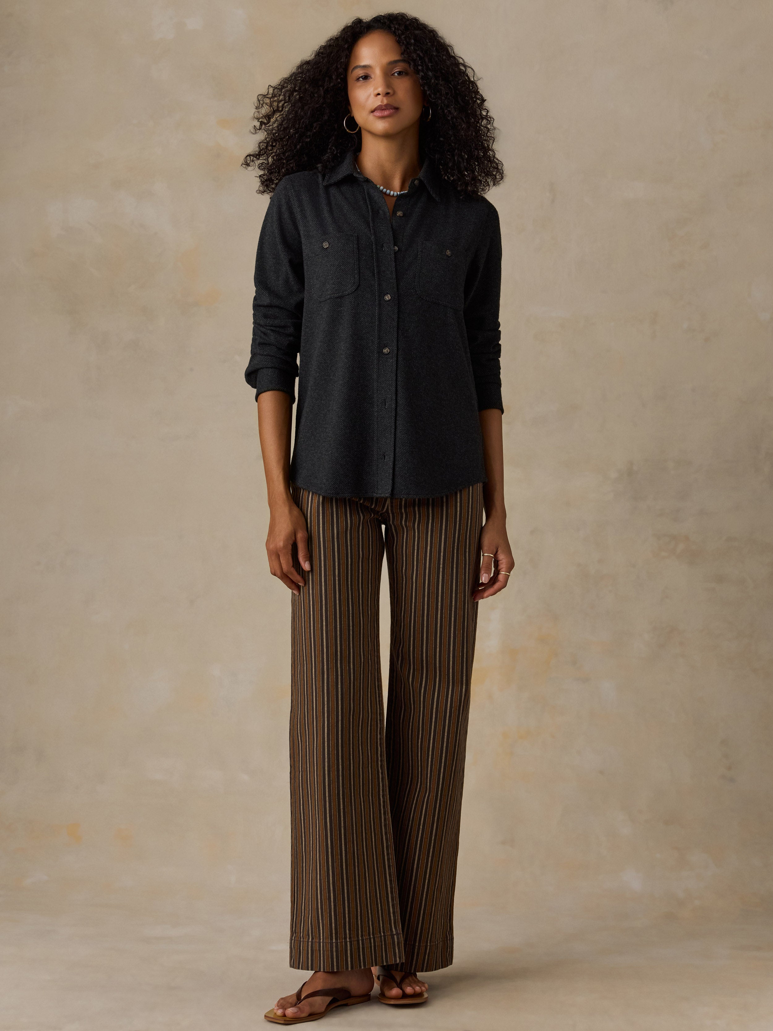 Woman wearing a black sweater shirt with brown striped pants against a beige background