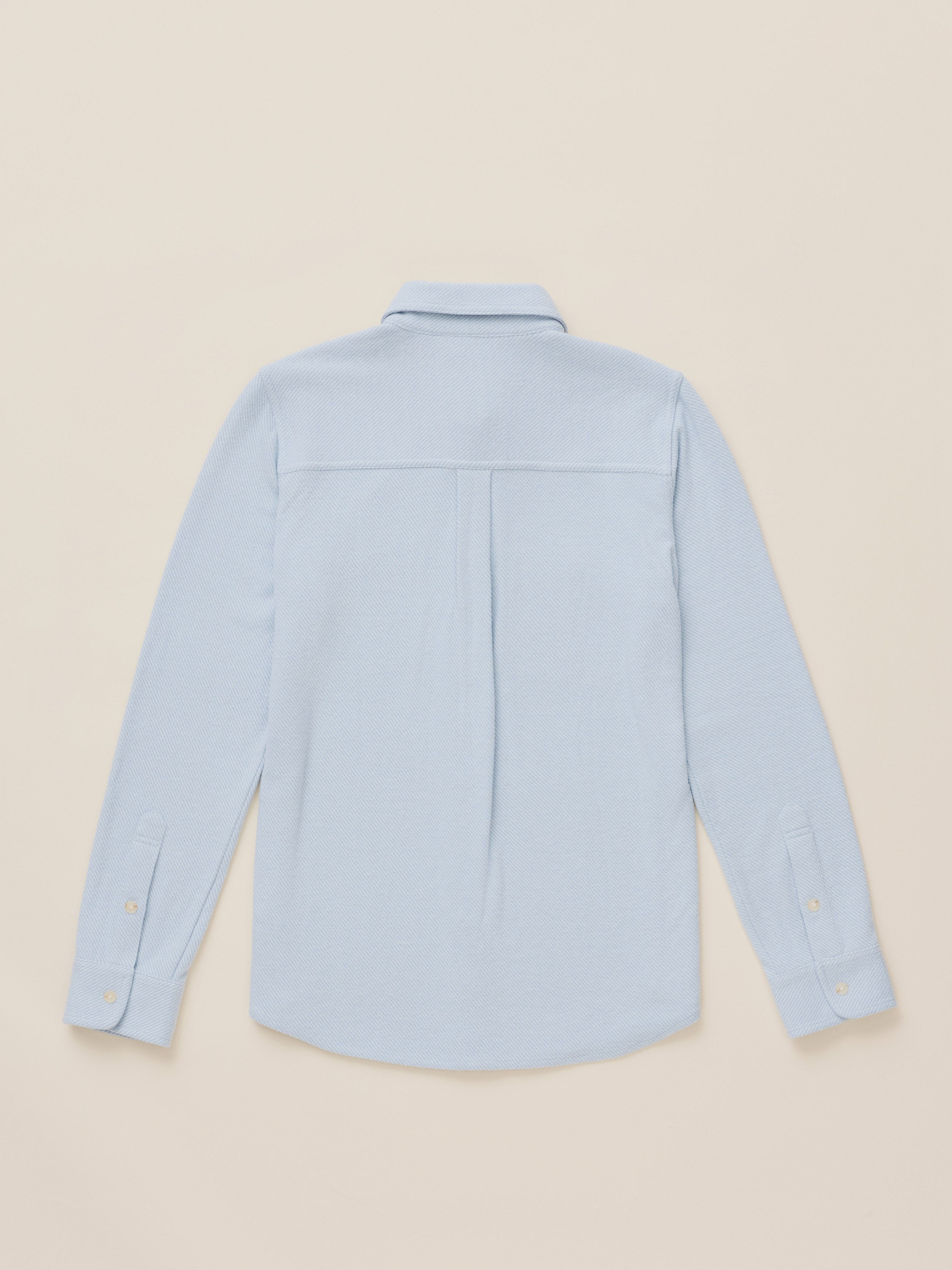 A light blue long-sleeve button-up shirt shown from the back, laid flat against a solid beige background.