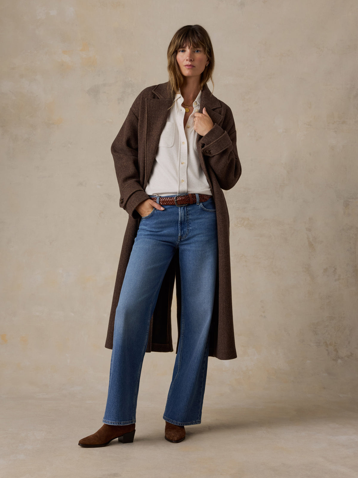 A woman wearing a brown jacket, white shirt, and blue jeans, image 5 of 7