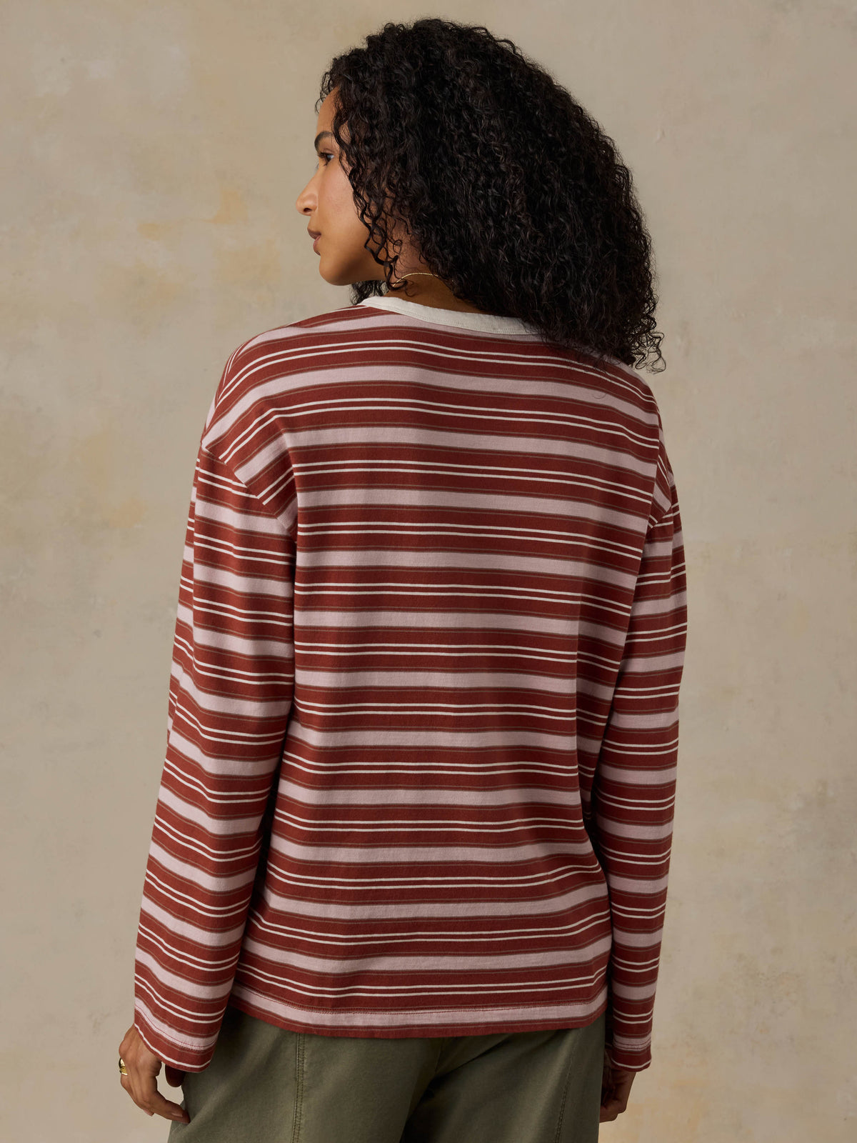 Woman wearing a red and pink striped long-sleeve shirt and green pants against a beige background, image 3 of 7