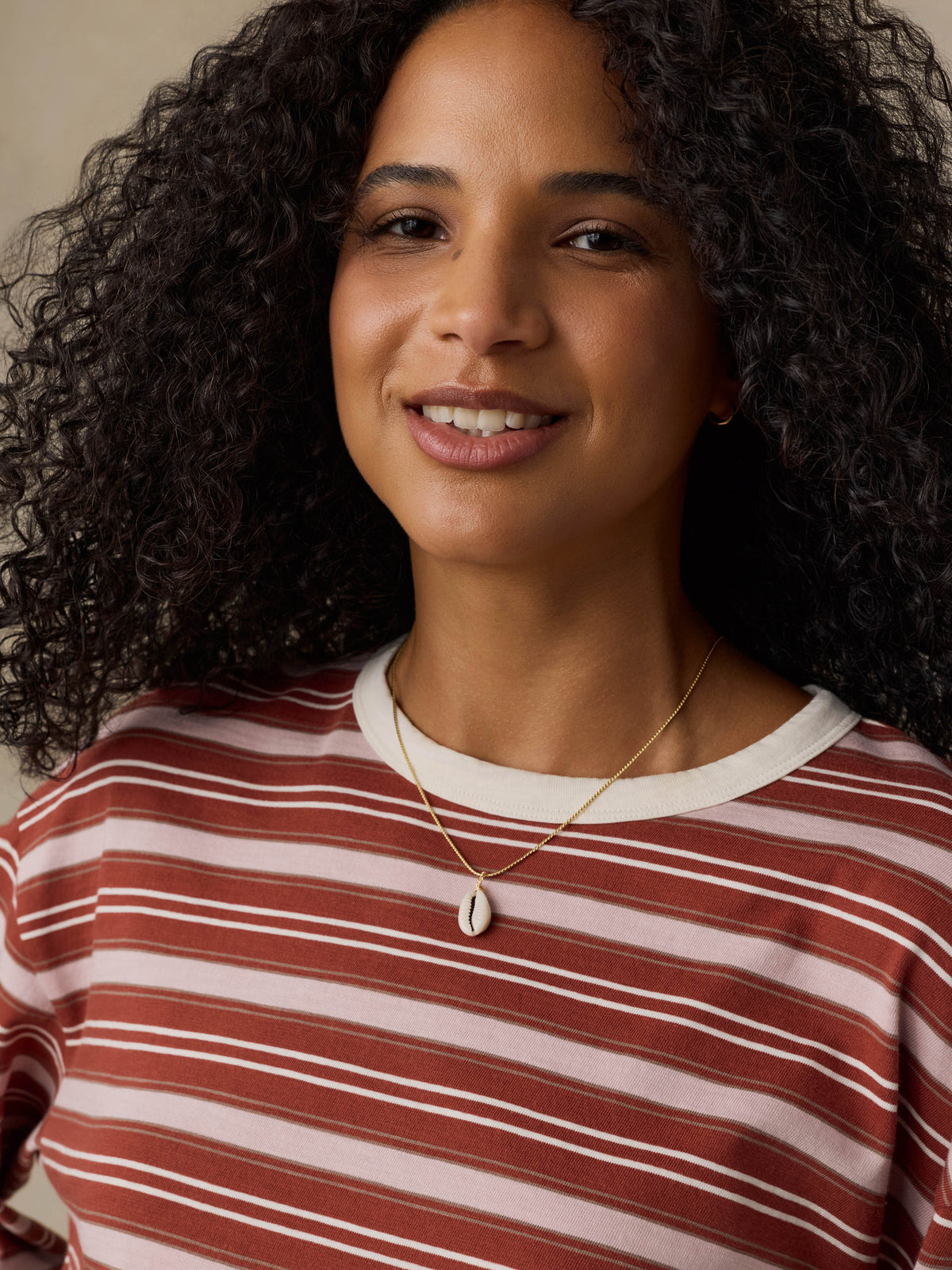 Woman wearing a red and pink striped long-sleeve shirt against a beige background, image 5 of 7