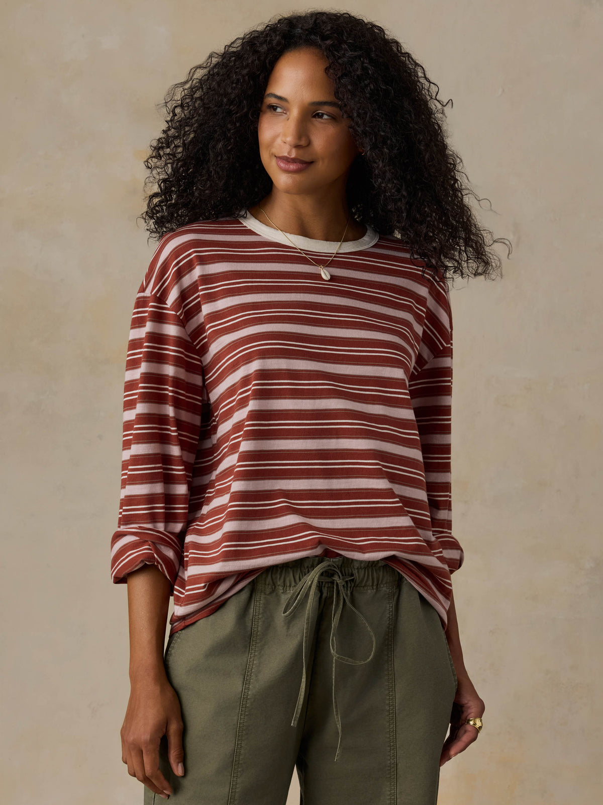 Woman wearing a red and pink striped long-sleeve shirt and green pants against a beige background, image 2 of 7