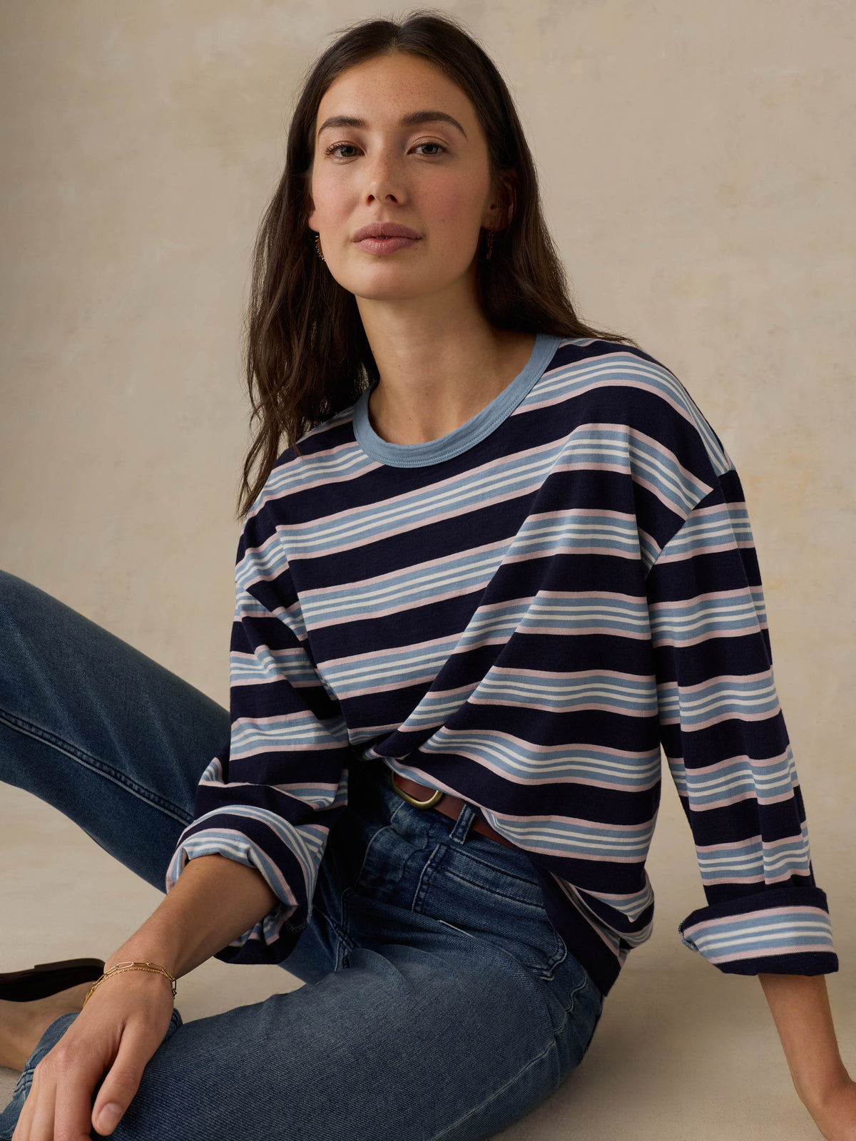 Woman wearing a blue striped shirt and jeans against a beige background, image 6 of 8