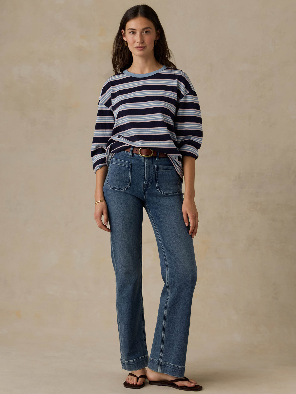 Woman wearing a blue striped shirt and jeans against a beige background, image 5 of 8