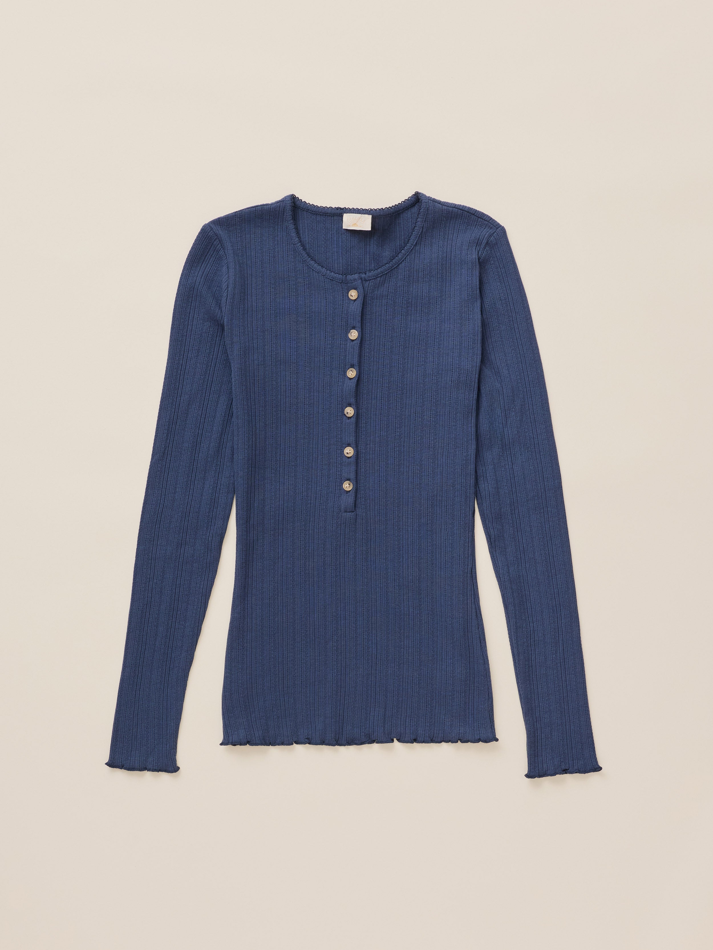 A long-sleeve ribbed knit henley top in a muted blue color, featuring a buttoned placket with gold-toned buttons, laid flat against a light beige background.