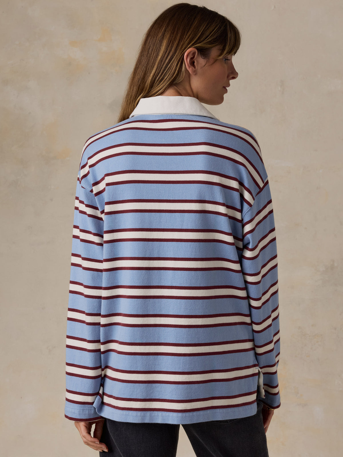 A woman wearing a light blue rugby sweater with burgundy and cream stripes, image 4 of 7