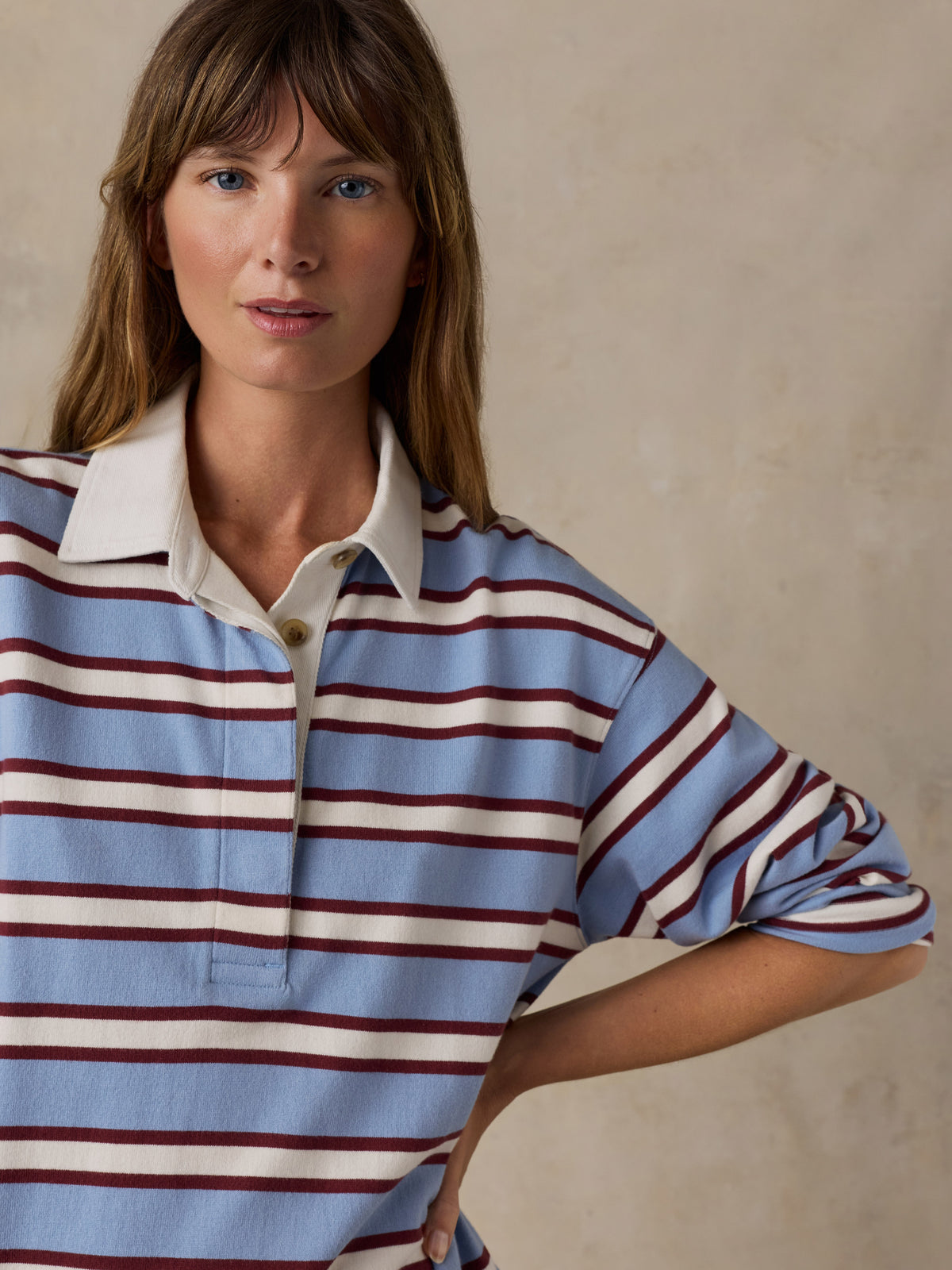 A woman wearing a rugby shirt with stripes in light blue, off-white, and dark red, image 5 of 7