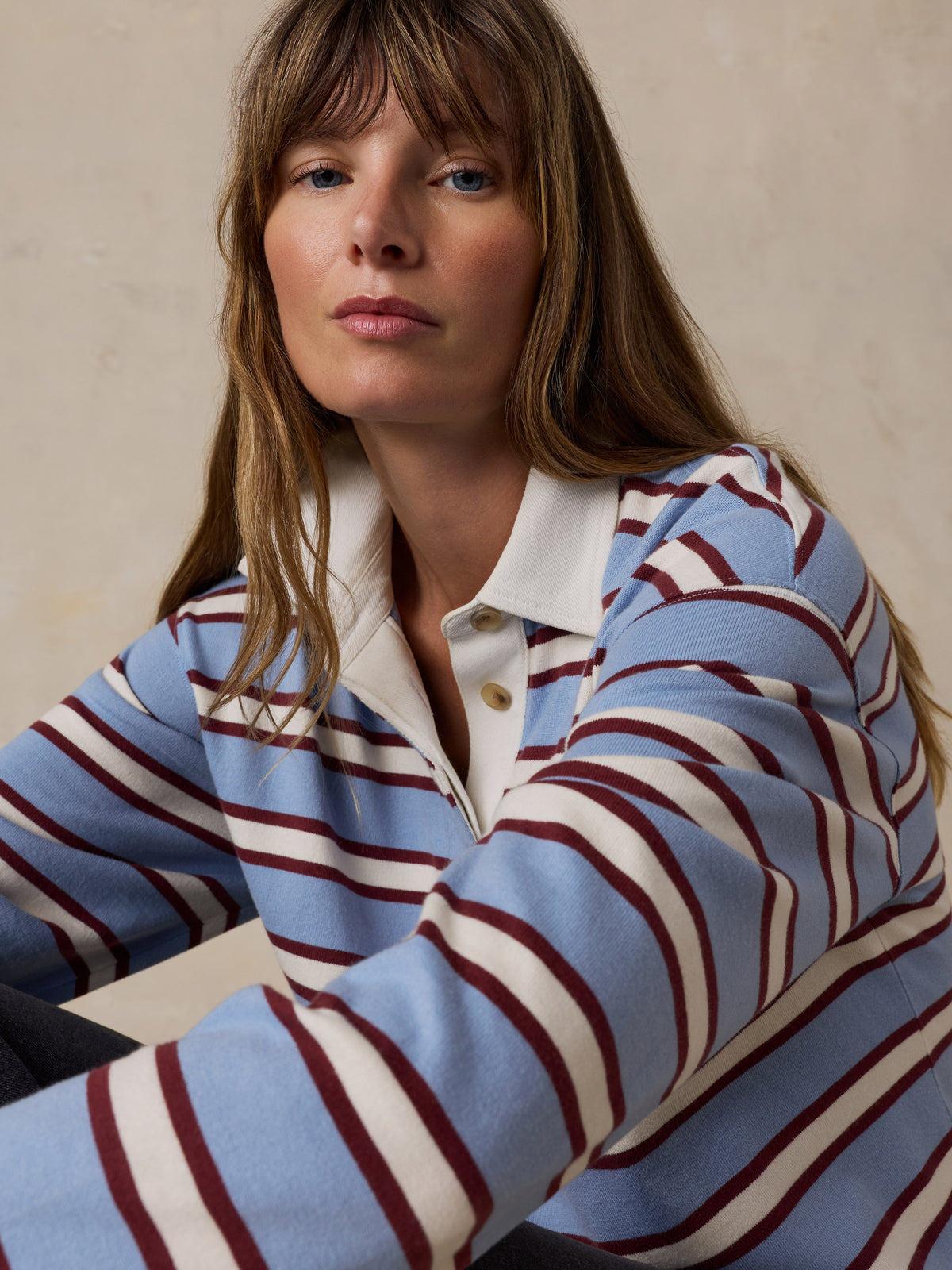 A woman wearing a light blue knit rugby shirt with burgundy and cream stripes, image 6 of 7