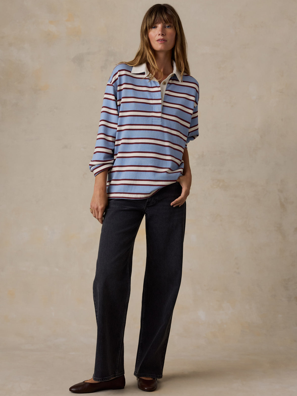 A woman wearing a light blue knit rugby shirt with burgundy and cream stripes and dark jeans, image 7 of 7