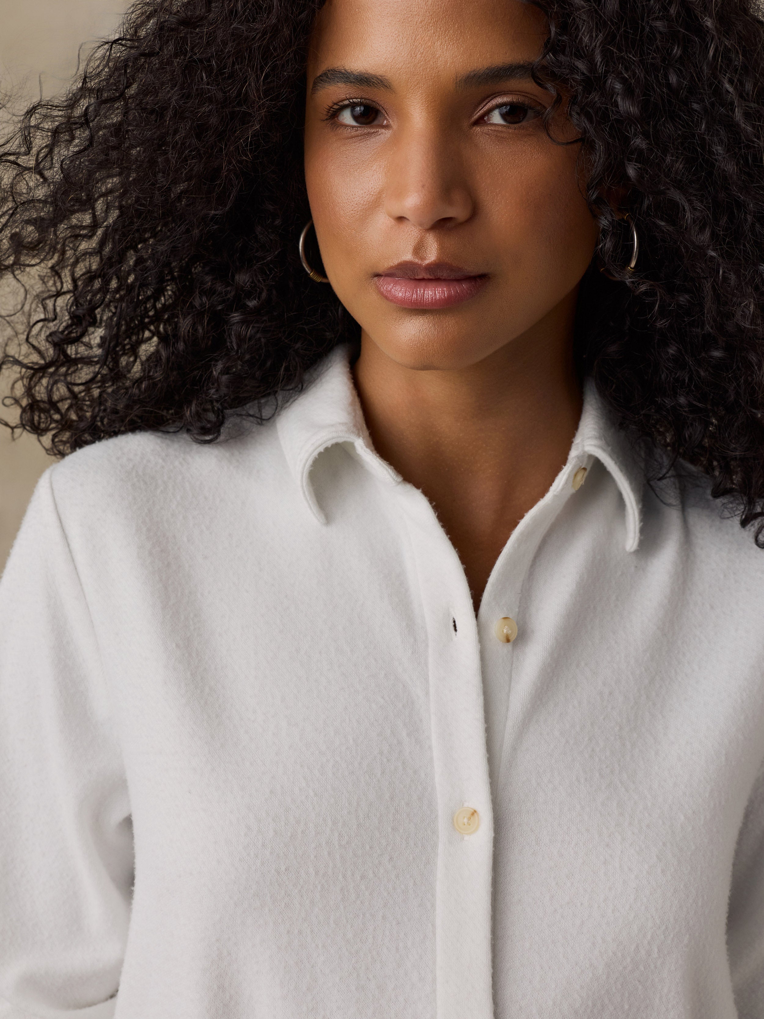 Woman wearing a white button up shirt against a beige background