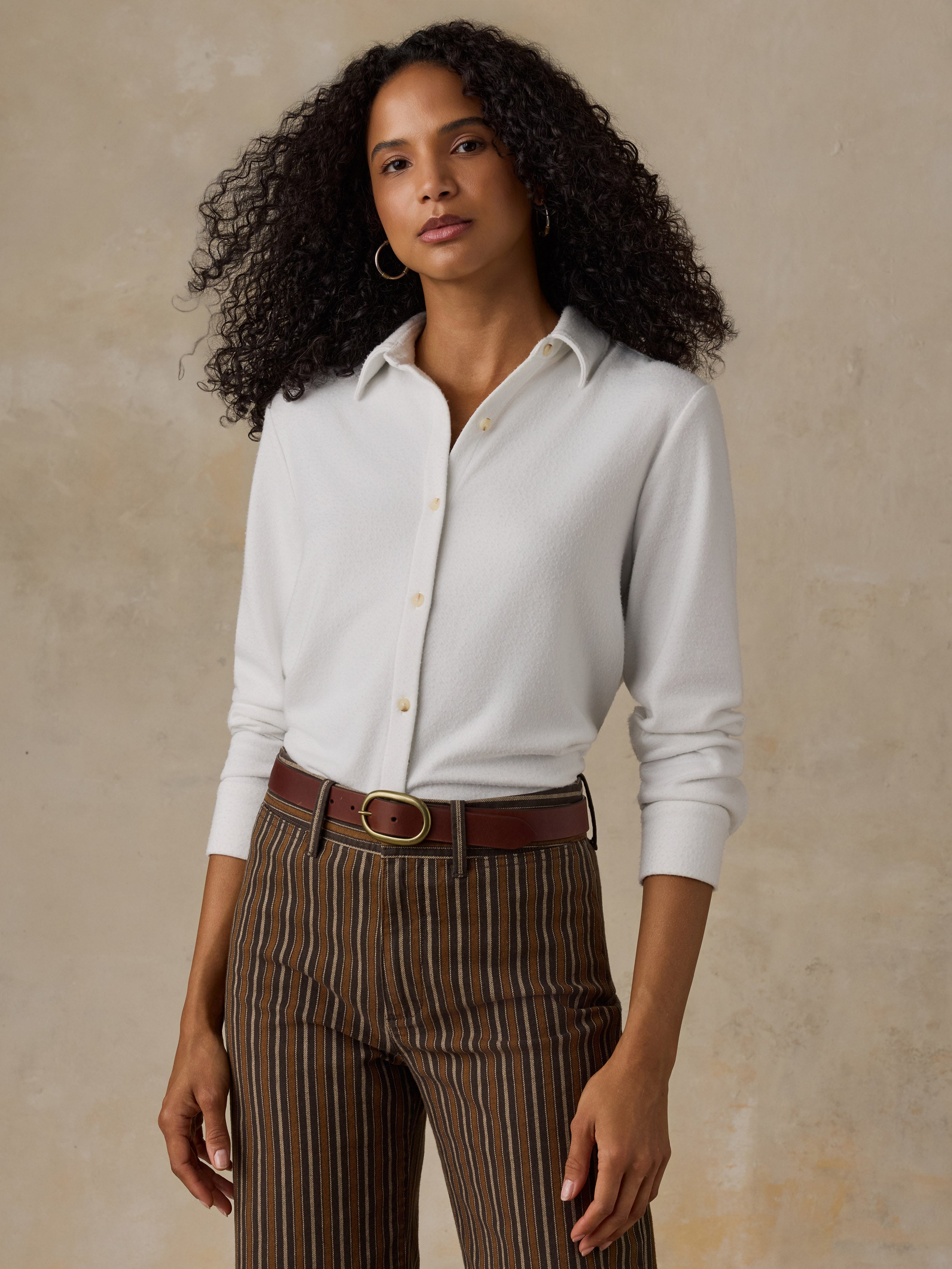 Woman wearing a white button up shirt and brown striped pants against a beige background