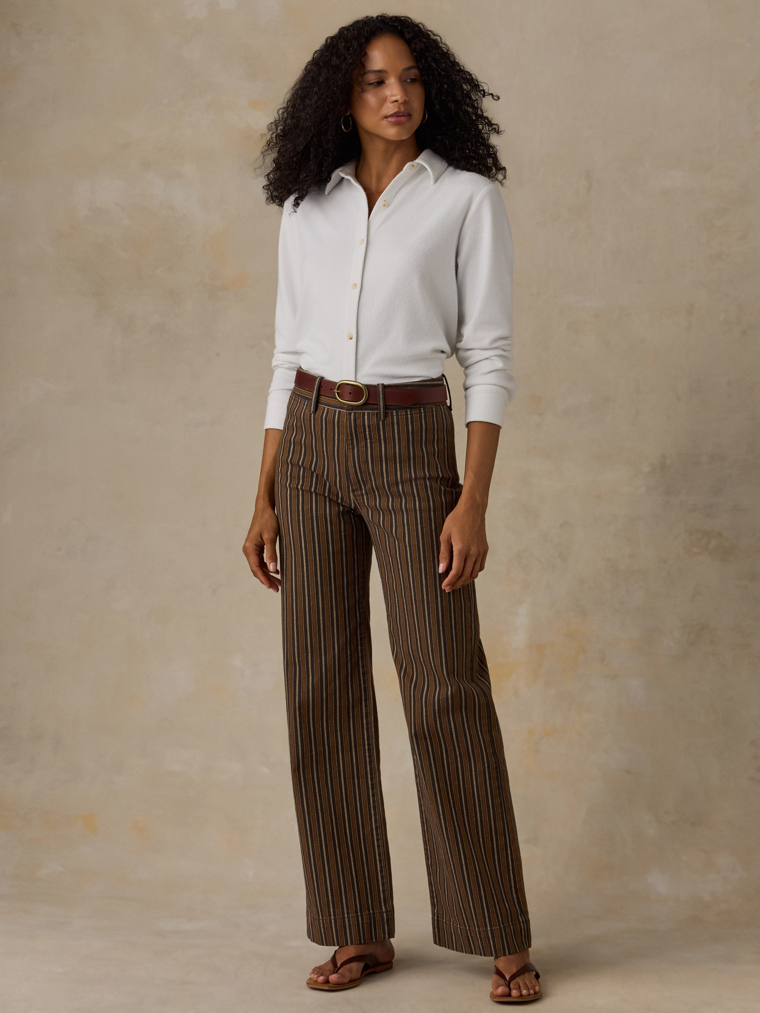 Woman wearing a white button up shirt and brown striped pants against a beige background