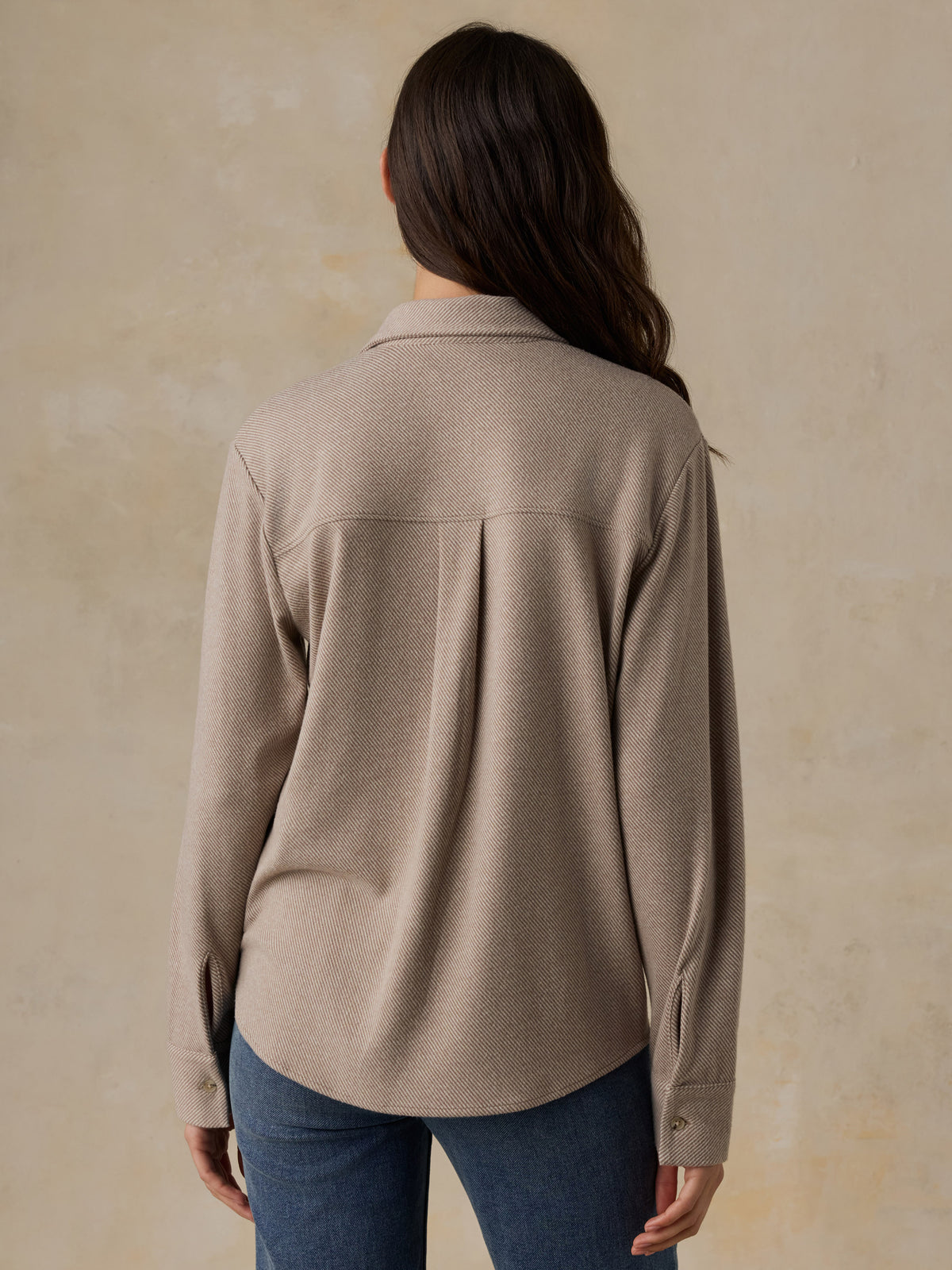 Woman wearing a beige button down shirt and blue jeans against a beige background, image 3 of 6