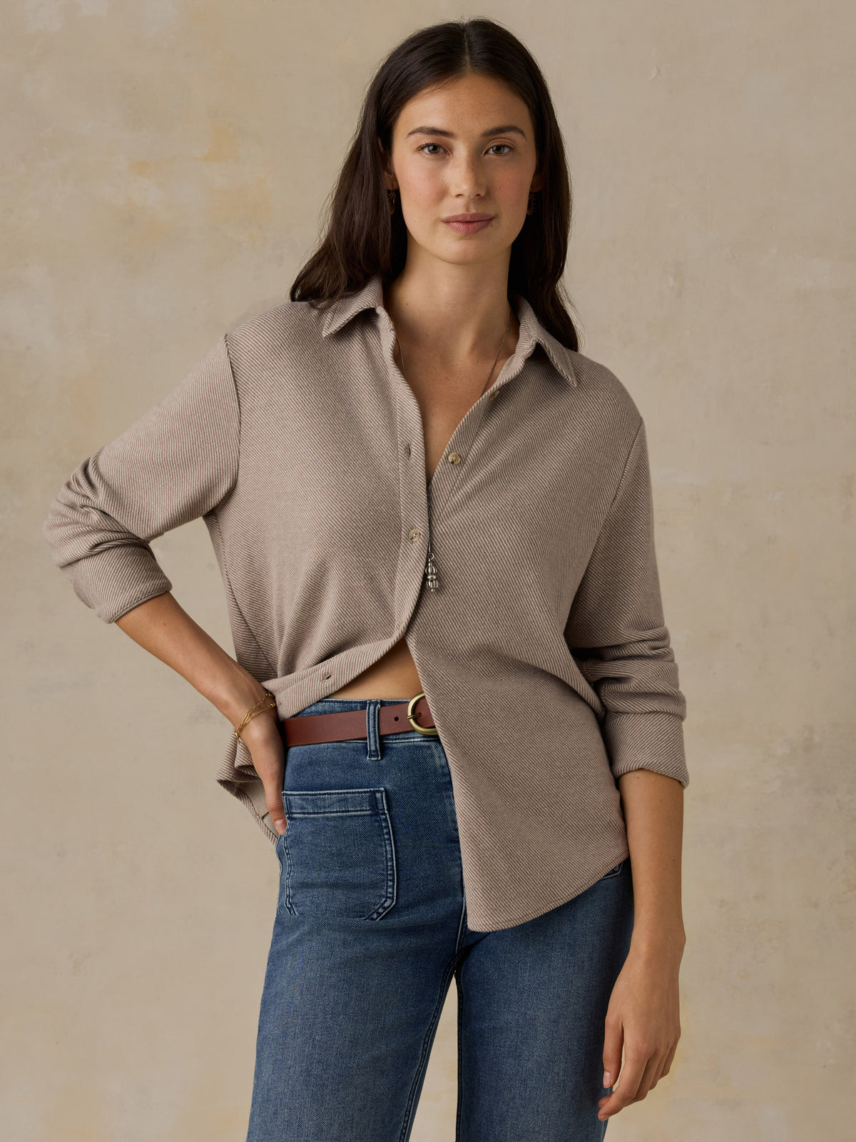 Woman wearing a beige button down shirt and blue jeans against a beige background, image 1 of 6