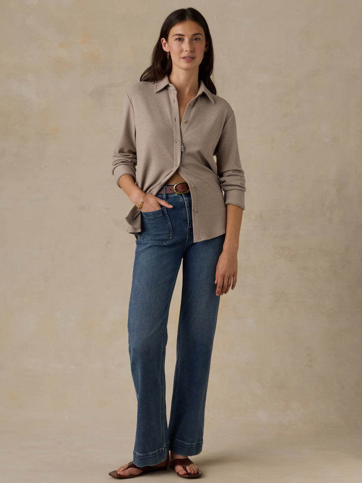 Woman wearing a beige button down shirt and blue jeans against a beige background, image 4 of 6