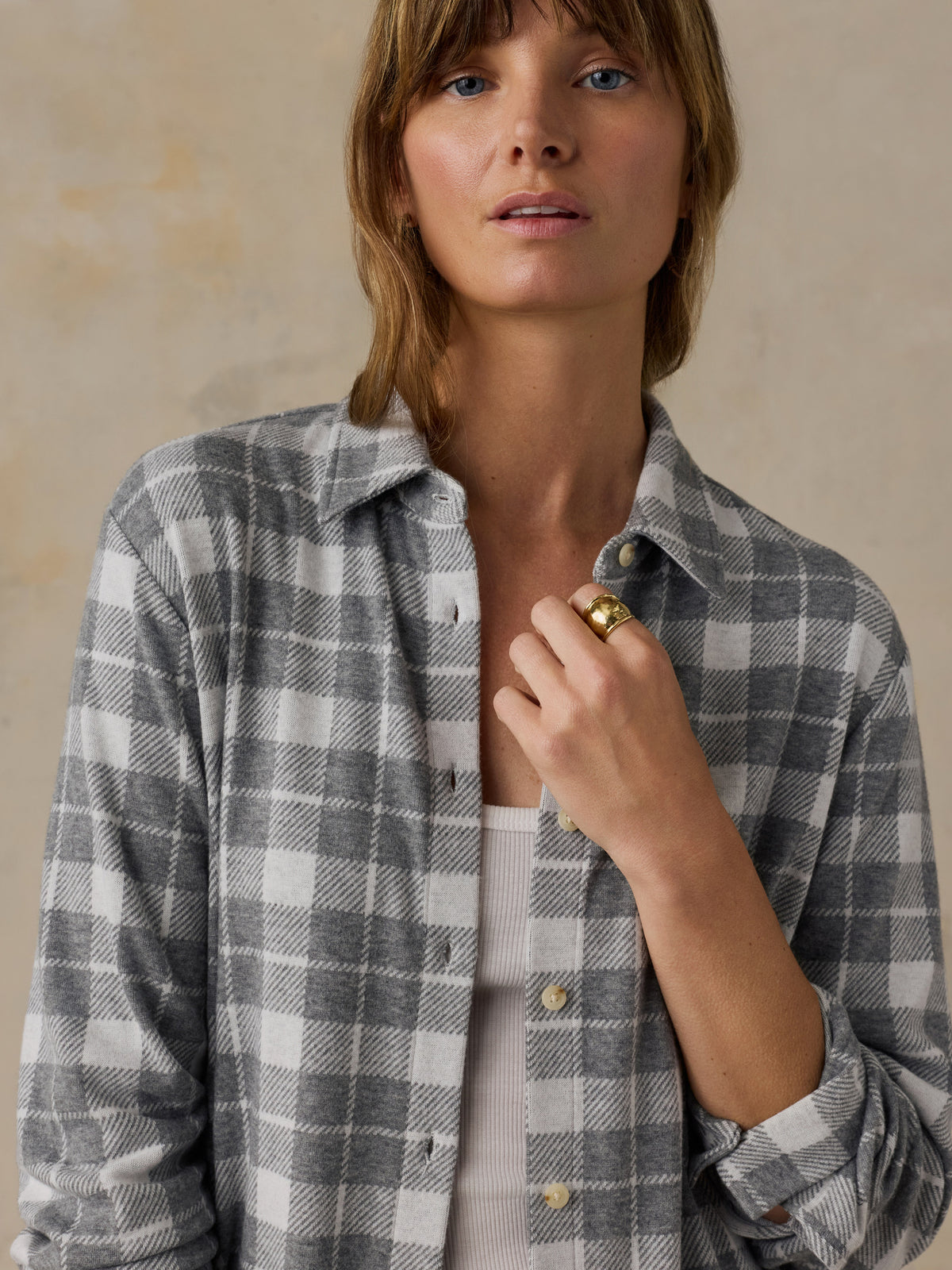 Woman wearing a grey plaid button down shirt against a beige background, image 5 of 6
