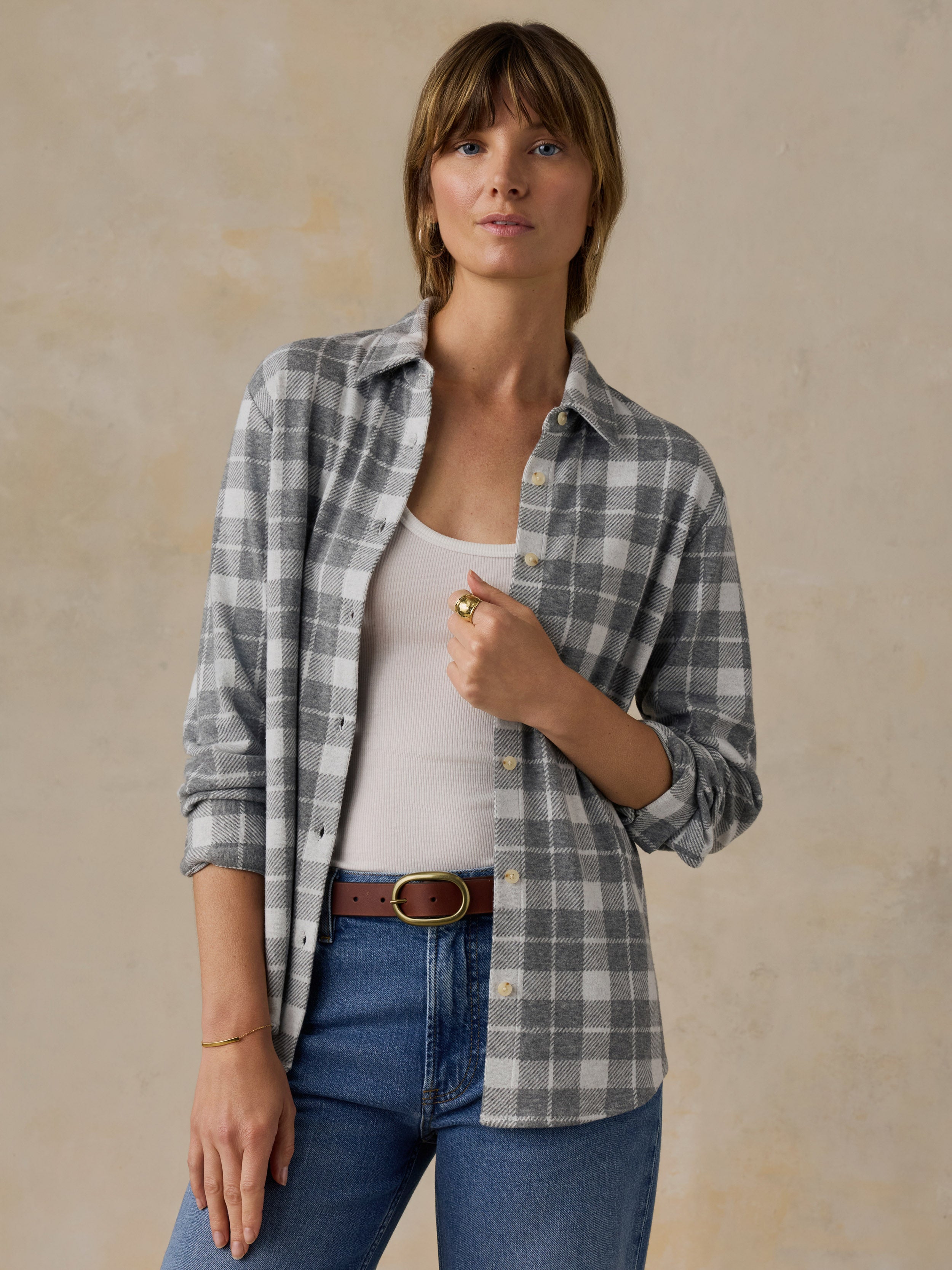 Woman wearing a grey plaid button down shirt and blue jeans against a beige background