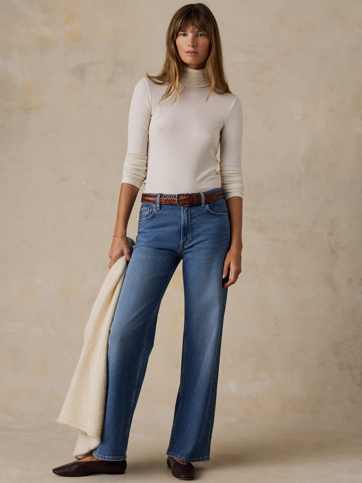 A woman wearing a white turtleneck, blue jeans, and black flats, image 5 of 7