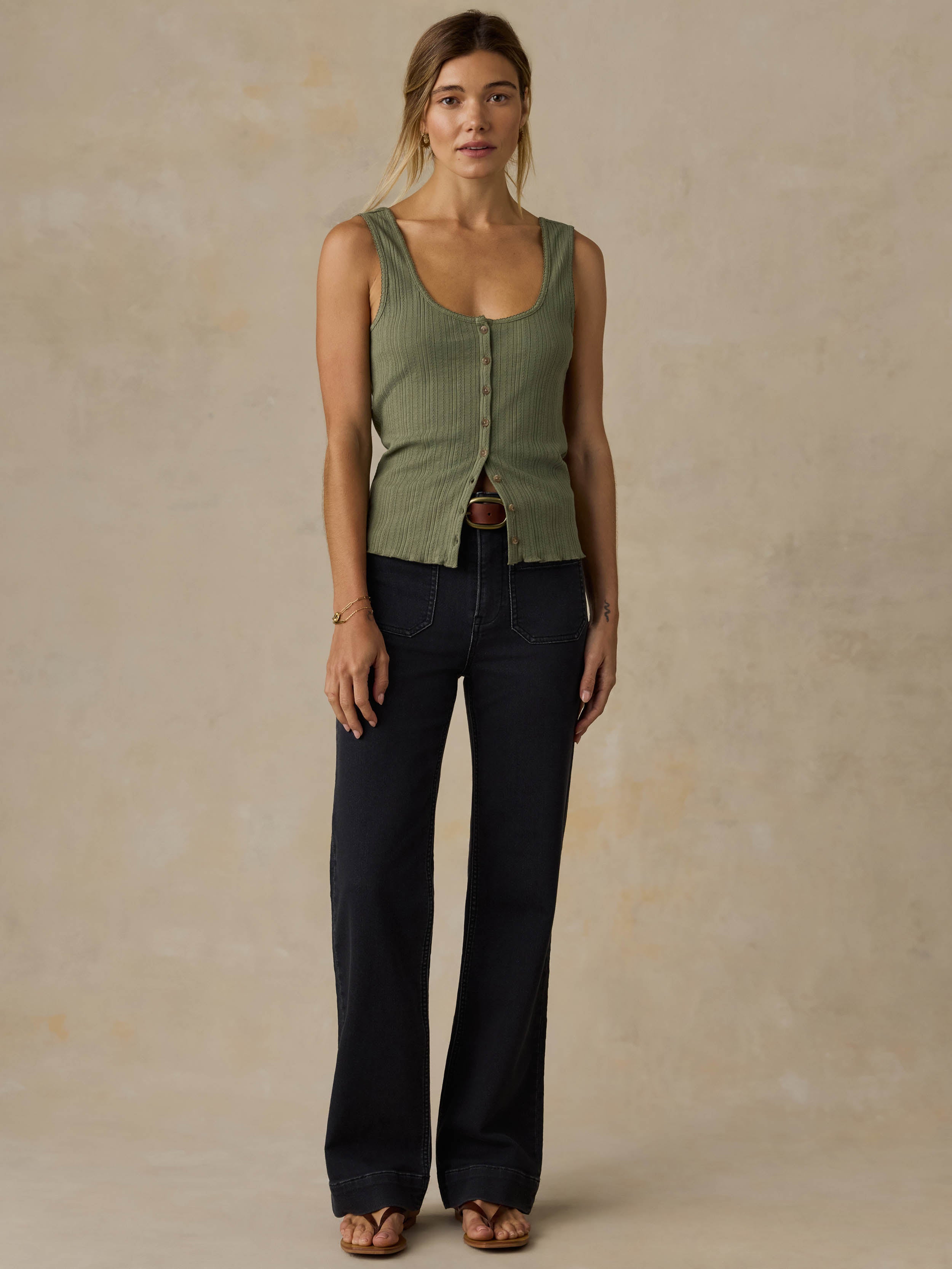 Woman wearing a green tank top and black jeans against a beige background