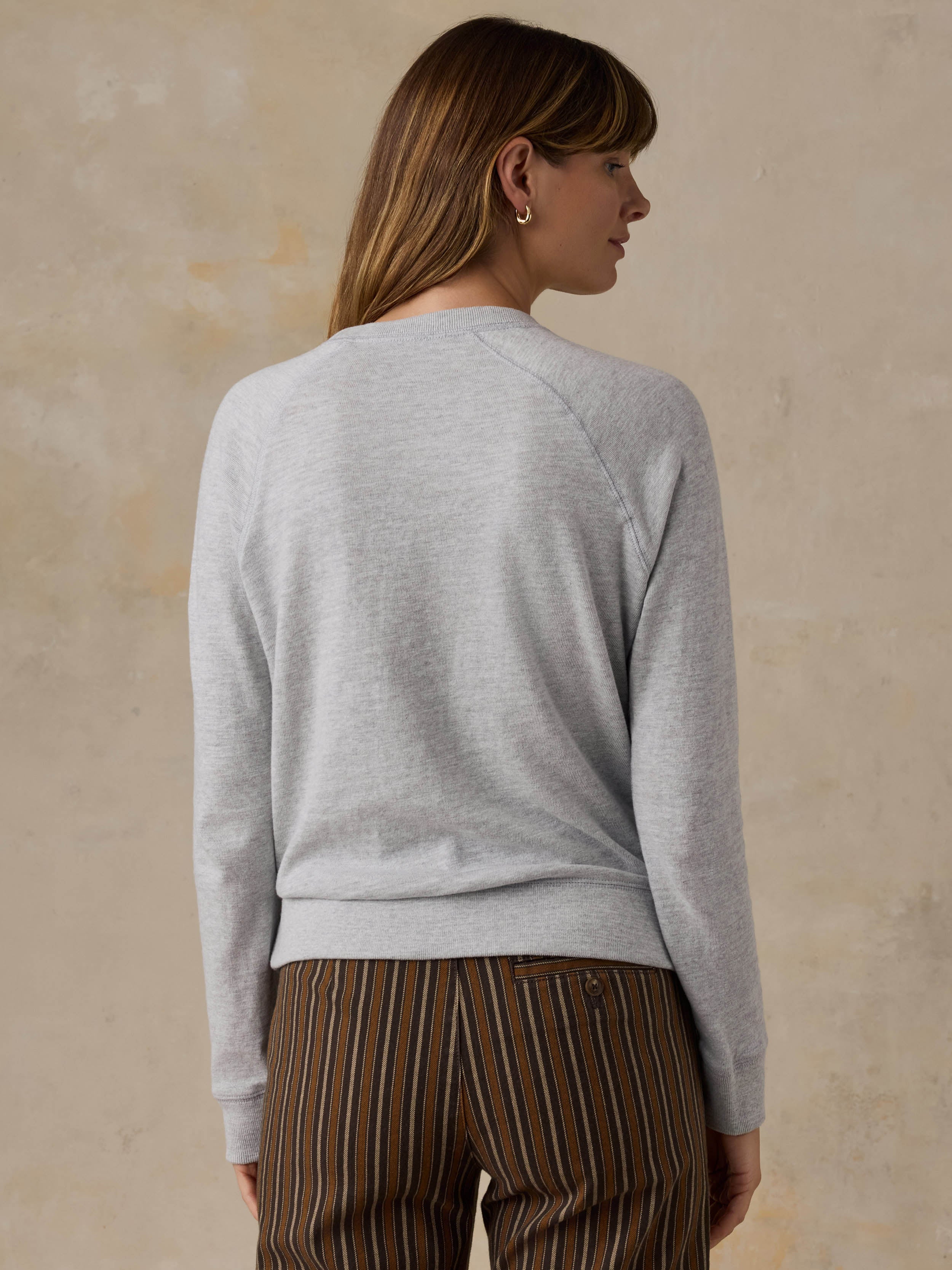 Woman wearing a grey crewneck with a National Parks graphic on the front against a beige background
