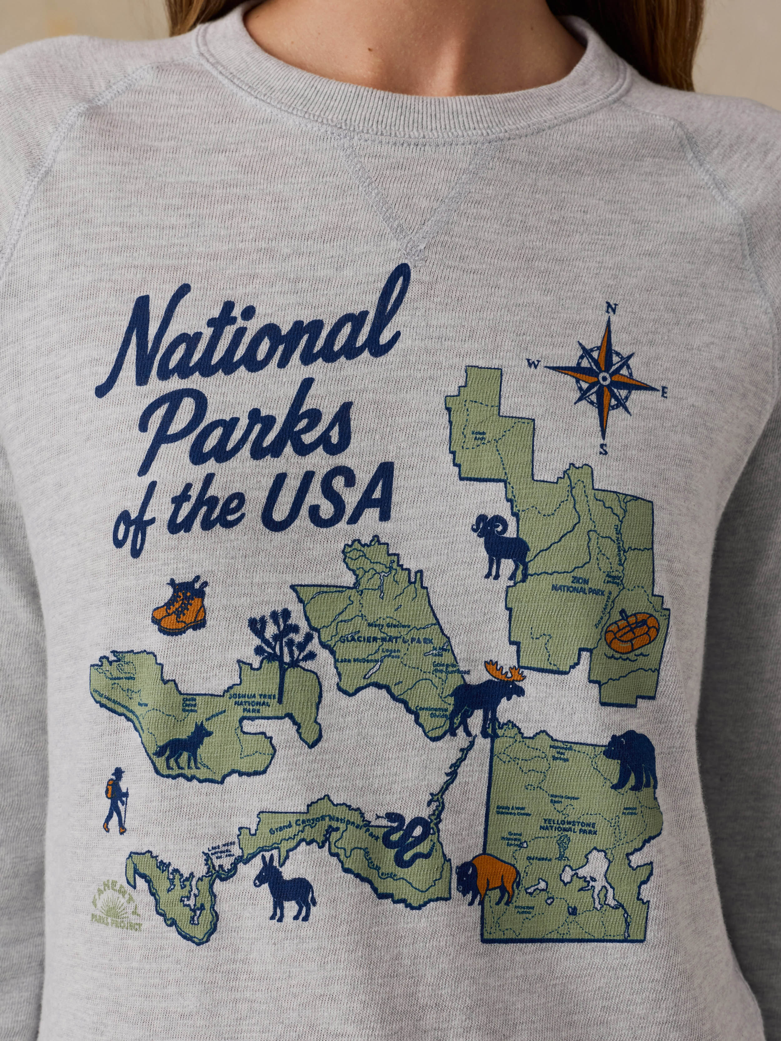 Woman wearing a grey crewneck with a National Parks graphic on the front against a beige background