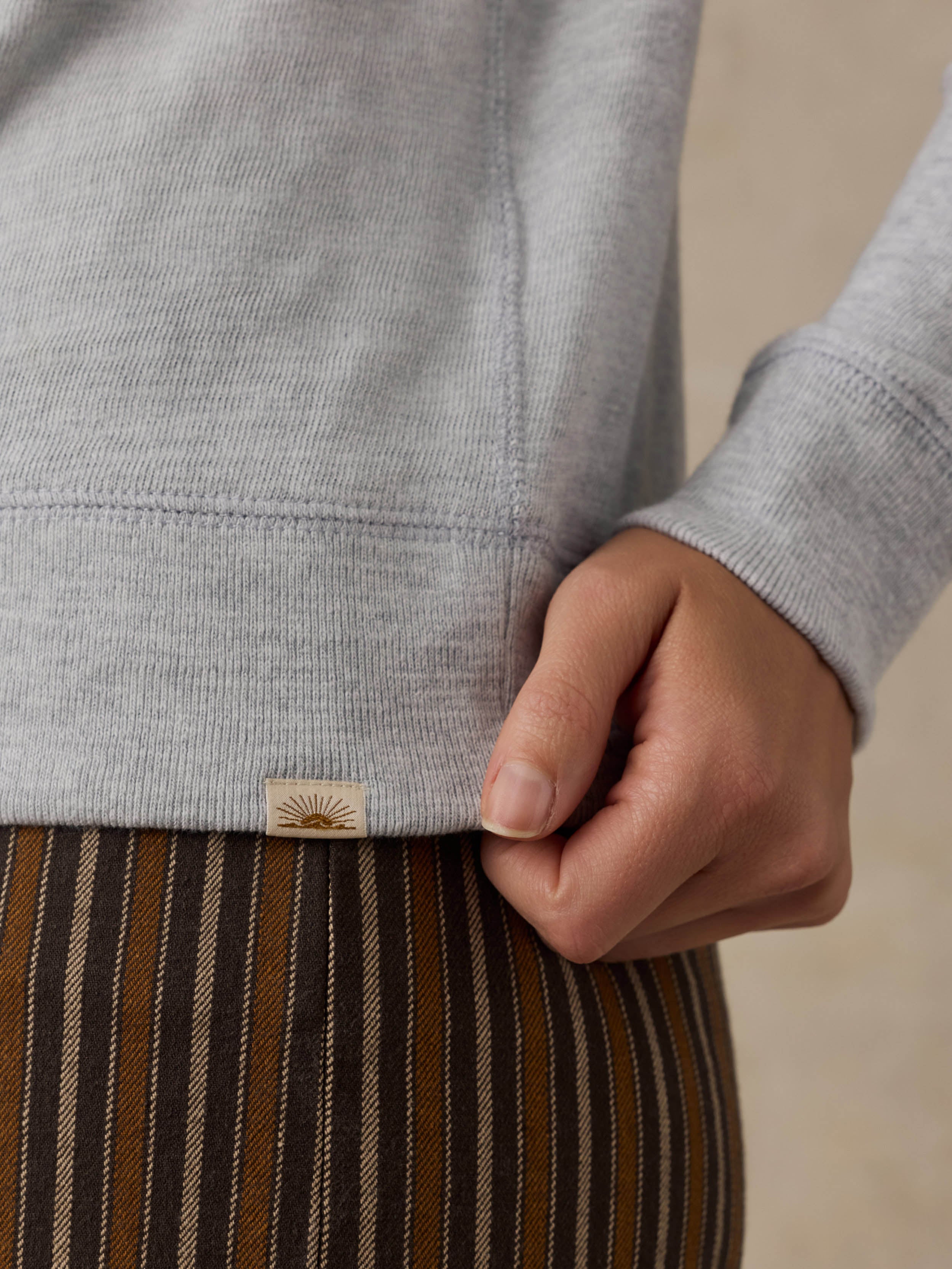 Close-up of a woman wearing a grey crewneck with a Faherty brand label at the hem