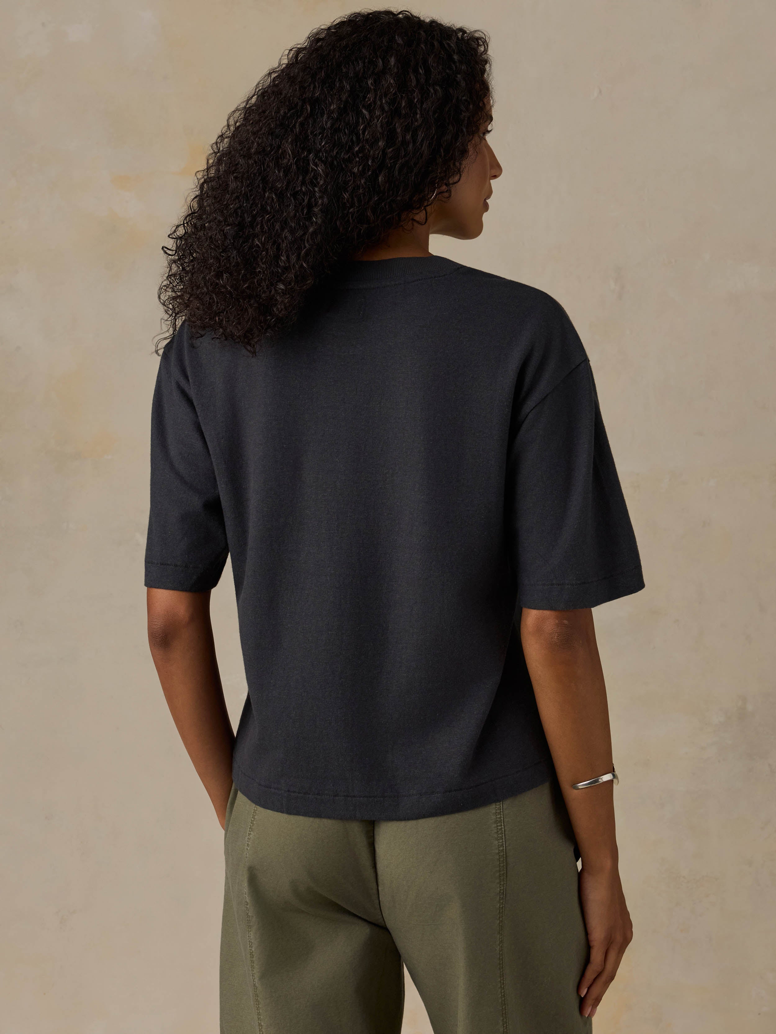Woman wearing a black t-shirt and green pants against a beige background