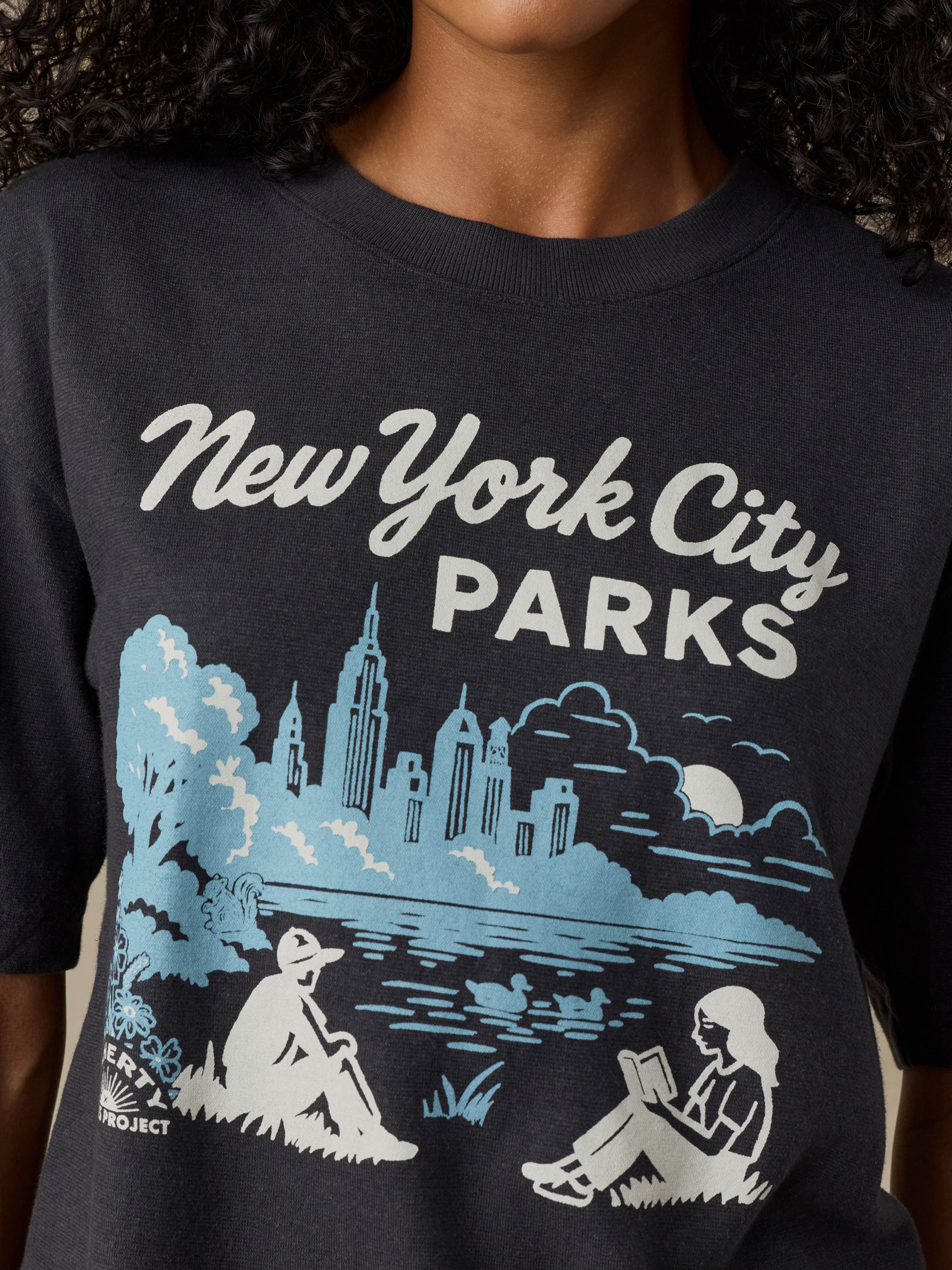 Black t-shirt with 'New York City Parks' design featuring people by a lake and skyline.