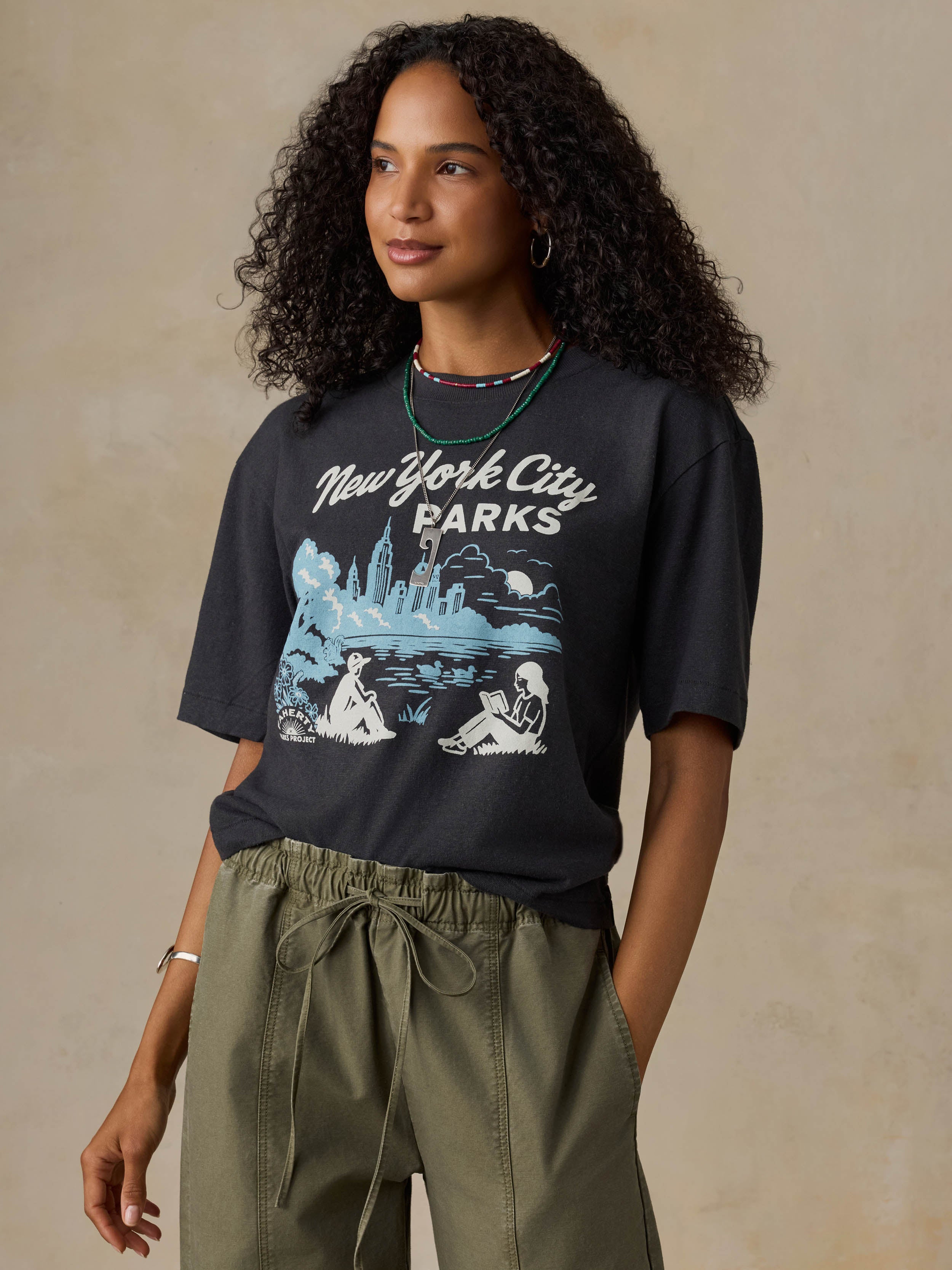 Woman wearing a black t-shirt with 'New York City Parks' graphic design on a beige background