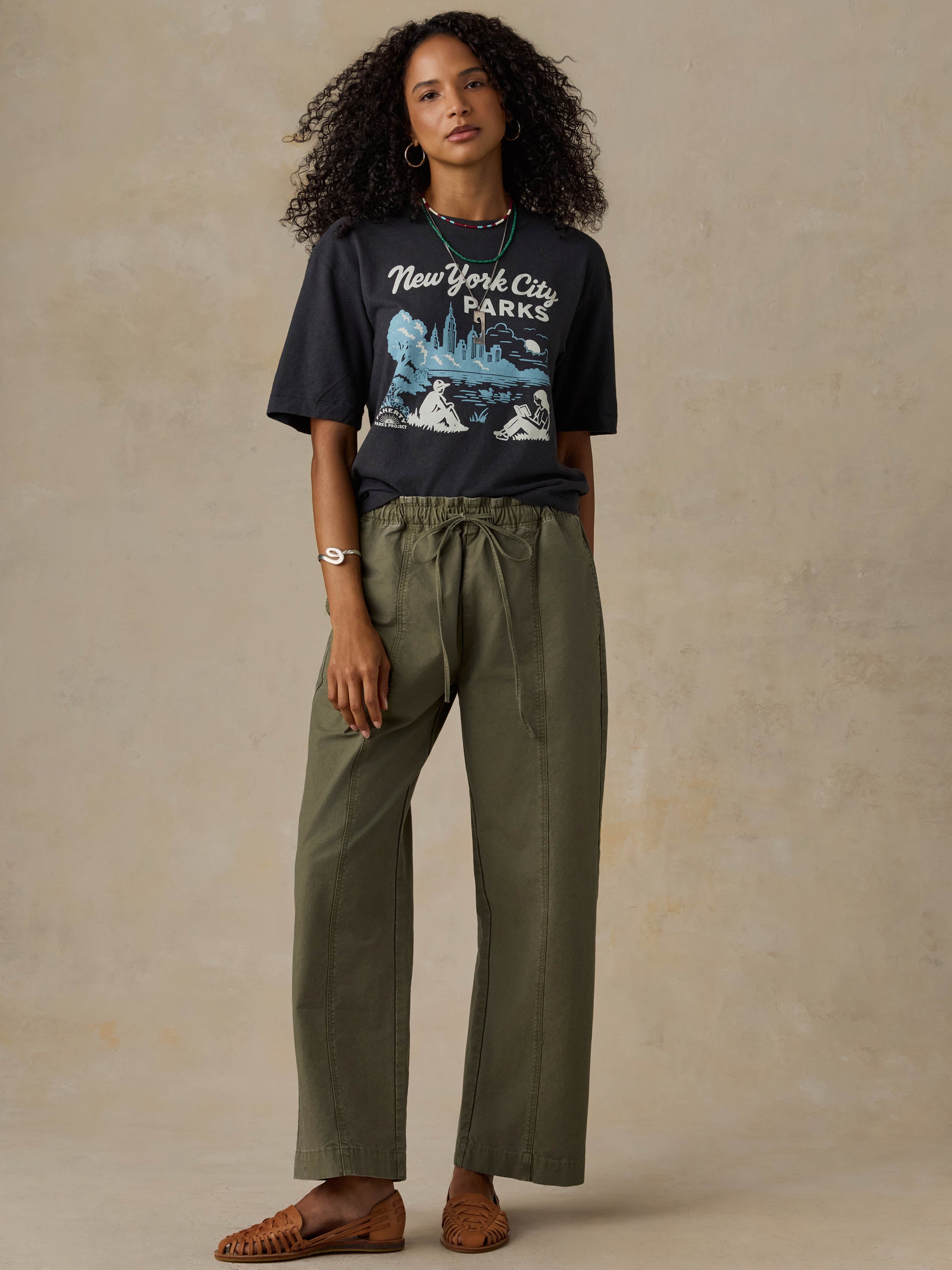 Woman wearing a black 'New York City Parks' t-shirt and green pants on a beige background