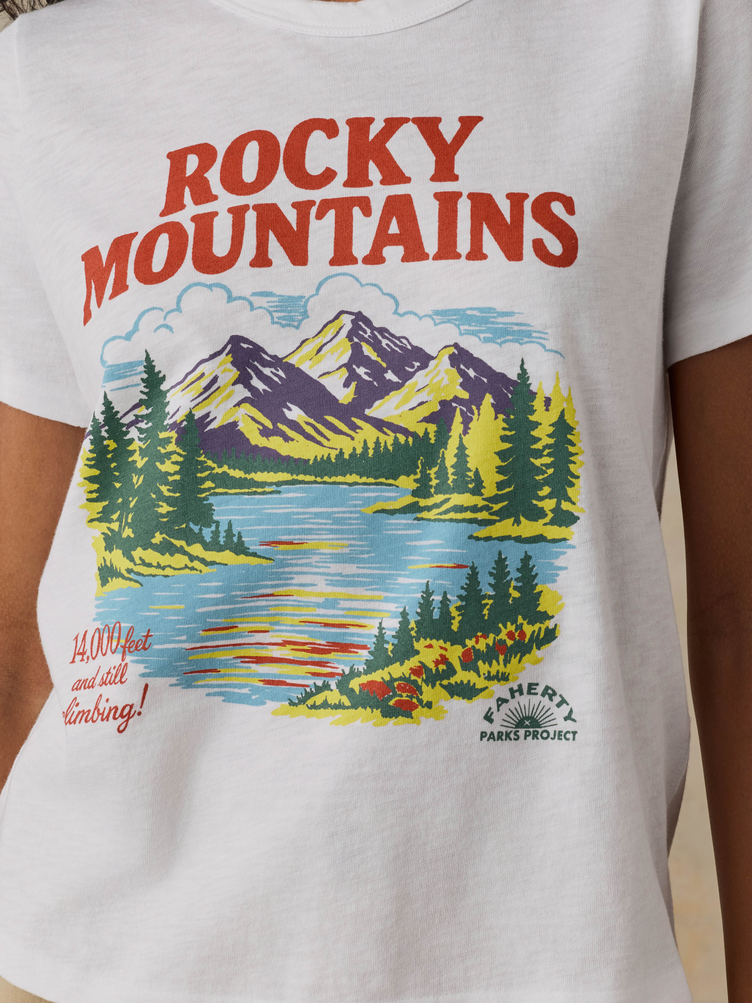 Woman wearing a white t-shirt with 'Rocky Mountains' design on a beige background