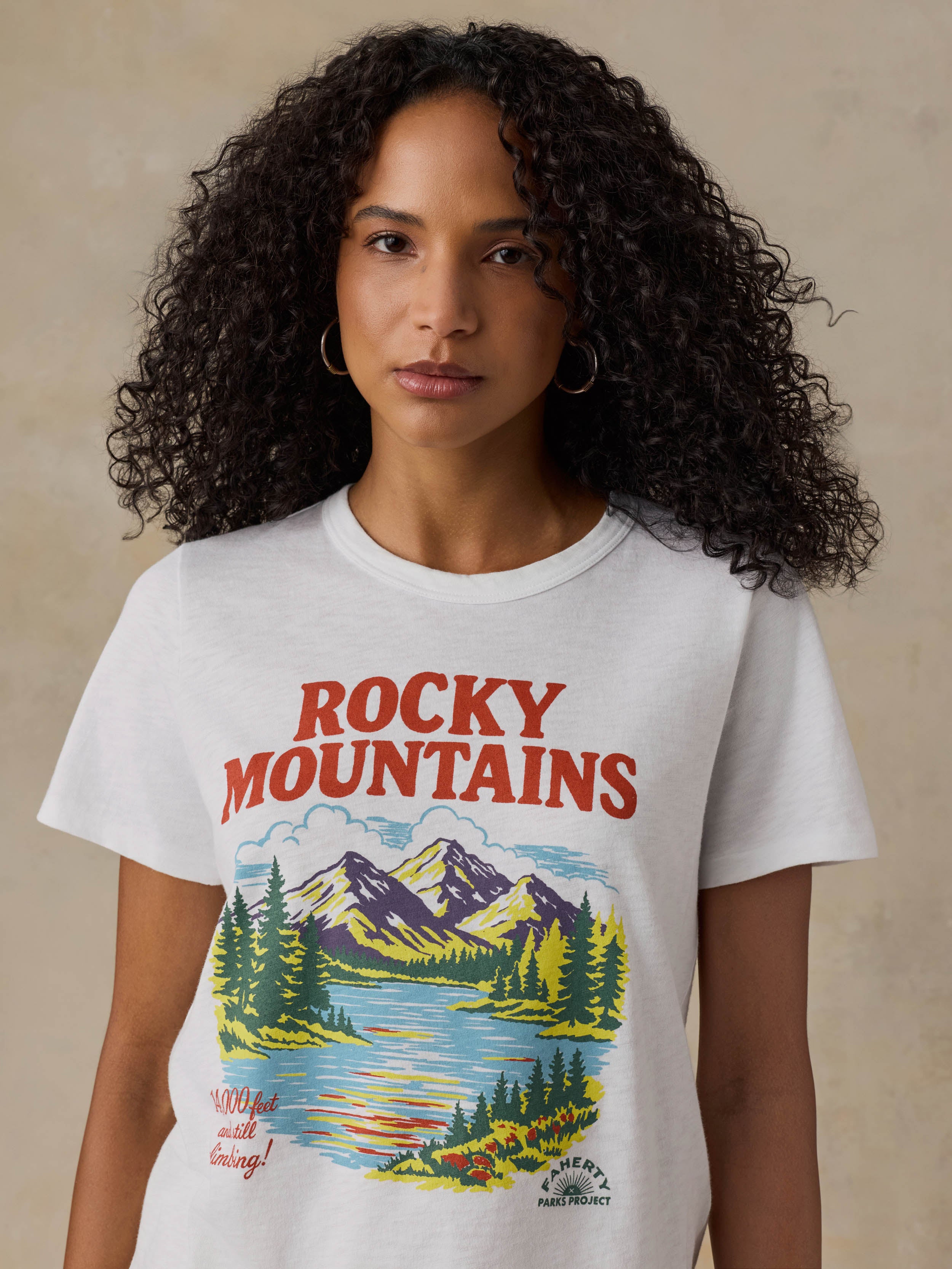 Woman wearing a white t-shirt with 'Rocky Mountains' design on a beige background