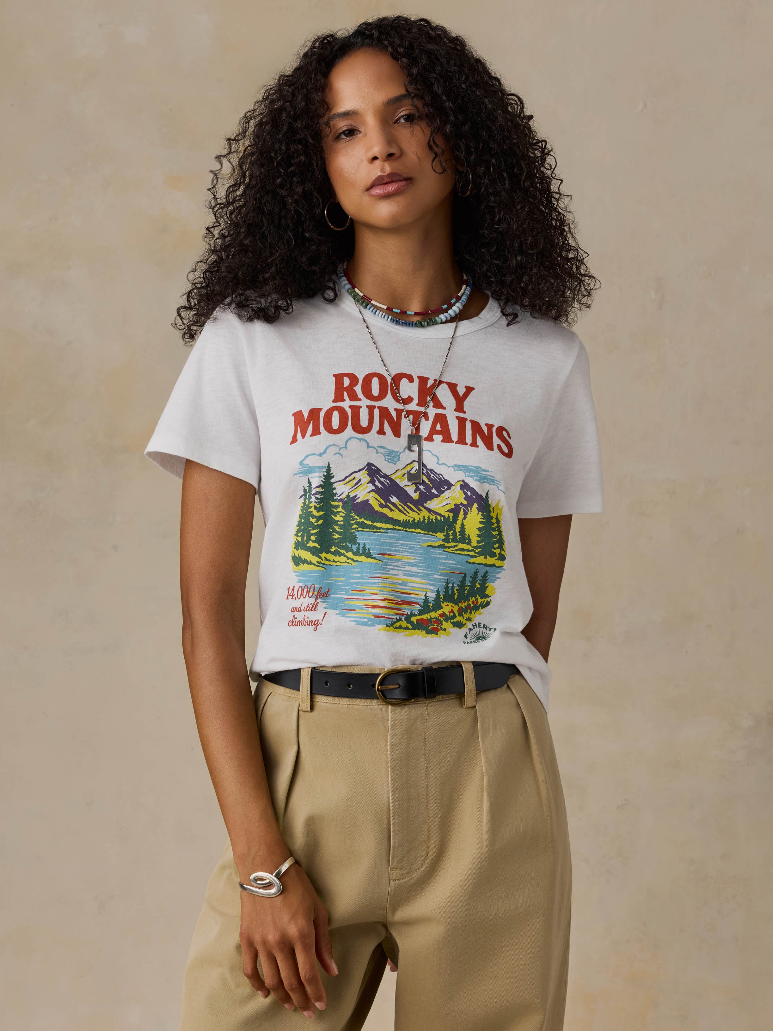 Woman wearing a white t-shirt with 'Rocky Mountains' design on a beige background