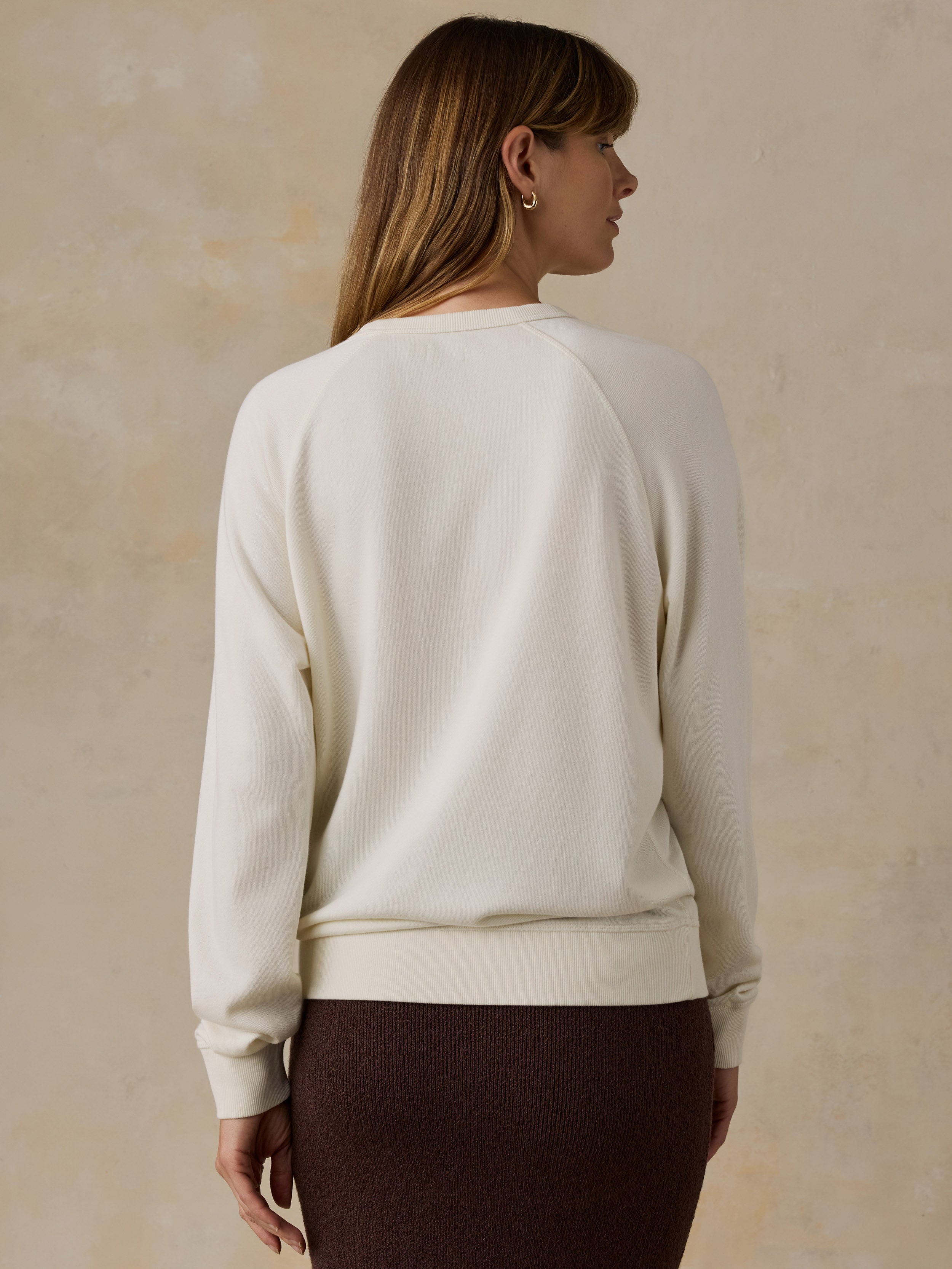 Woman wearing a Big Sur crewneck and brown skirt against a beige background