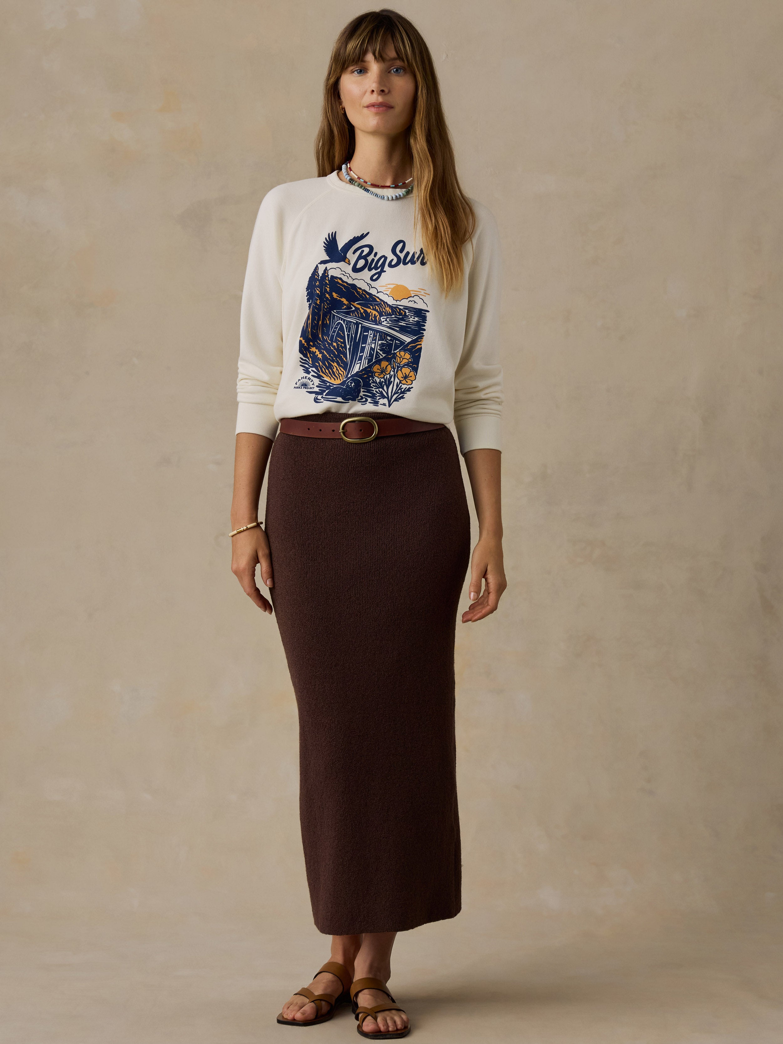 Woman wearing a Big Sur crewneck and brown skirt against a beige background