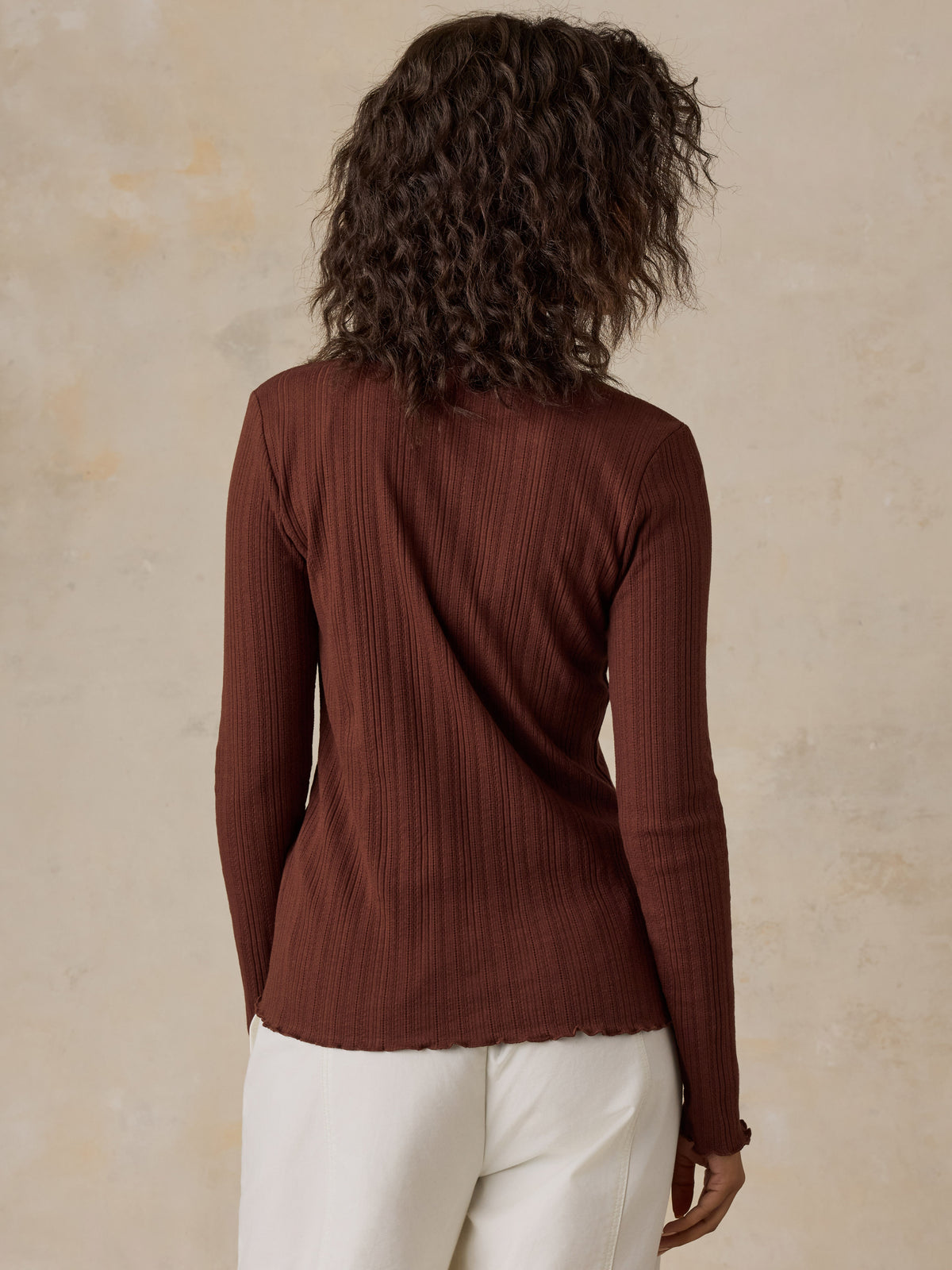A woman viewed from behind wearing a brown knit cardigan and white pants, image 3 of 6